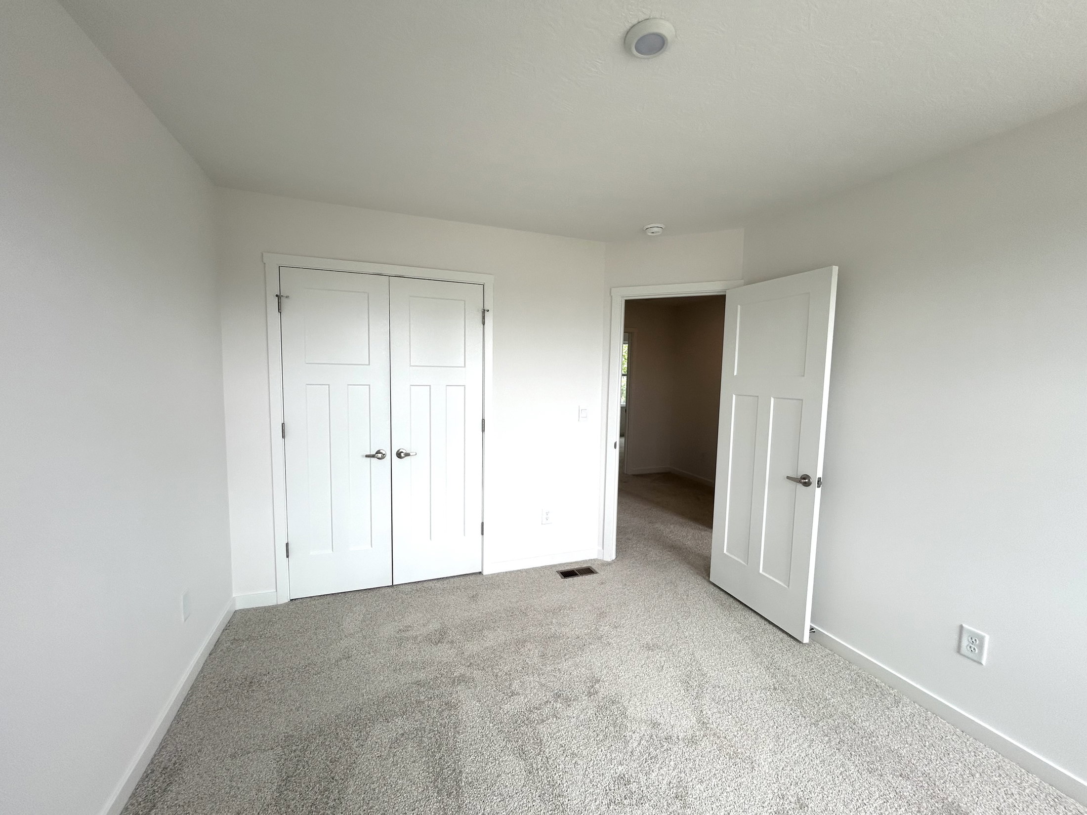 Modern, empty bedroom with carpet, white walls, and double closet doors.