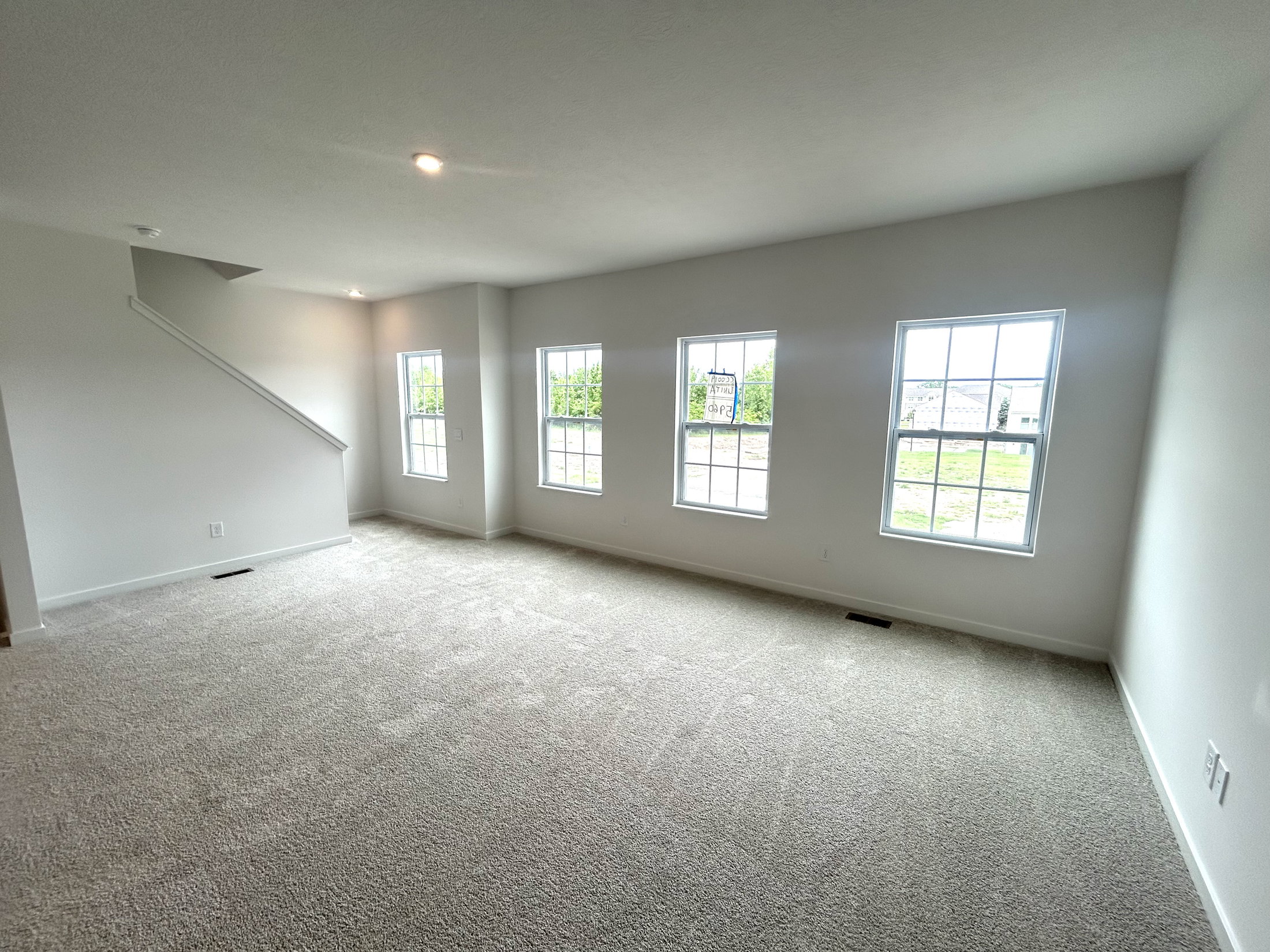 Bright and spacious living room with carpet flooring, white walls, and large windows providing ample natural light.