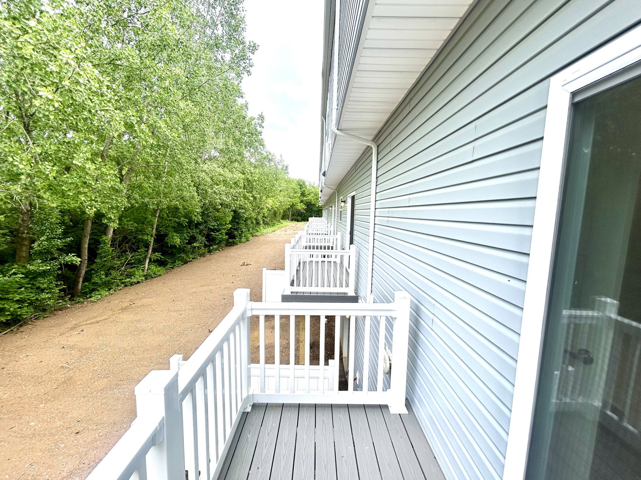 A serene view of a multi-unit building with white railings along a pathway surrounded by lush greenery.