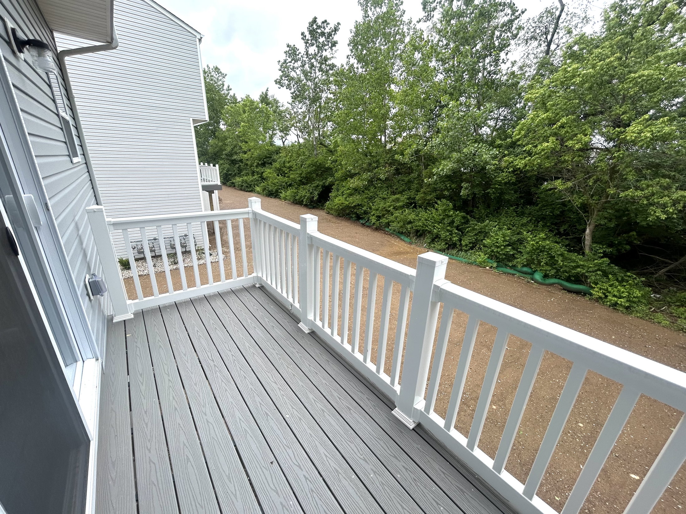 A modern deck with white railings overlooking a gravel path and lush green trees.