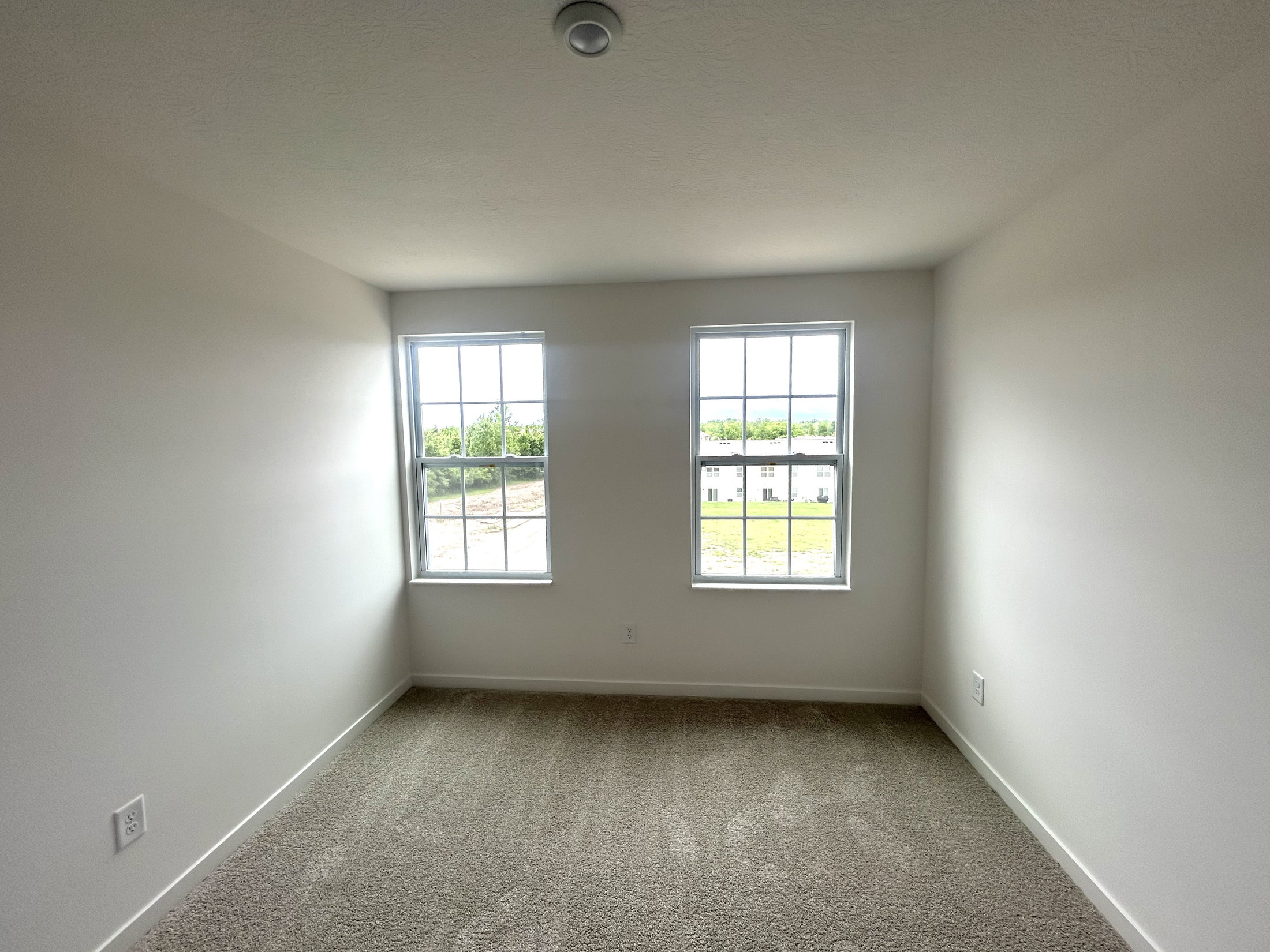 Bright and spacious empty bedroom with two windows and light-colored carpet.