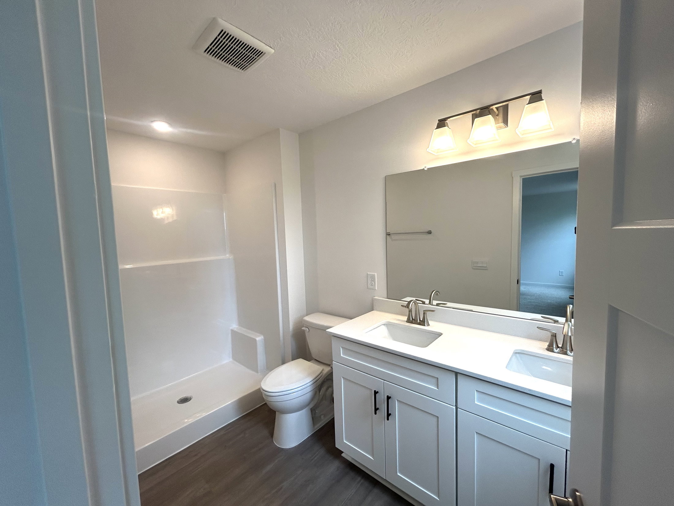 Bright and modern bathroom featuring a dual sink vanity, spacious shower area, and contemporary lighting fixtures.