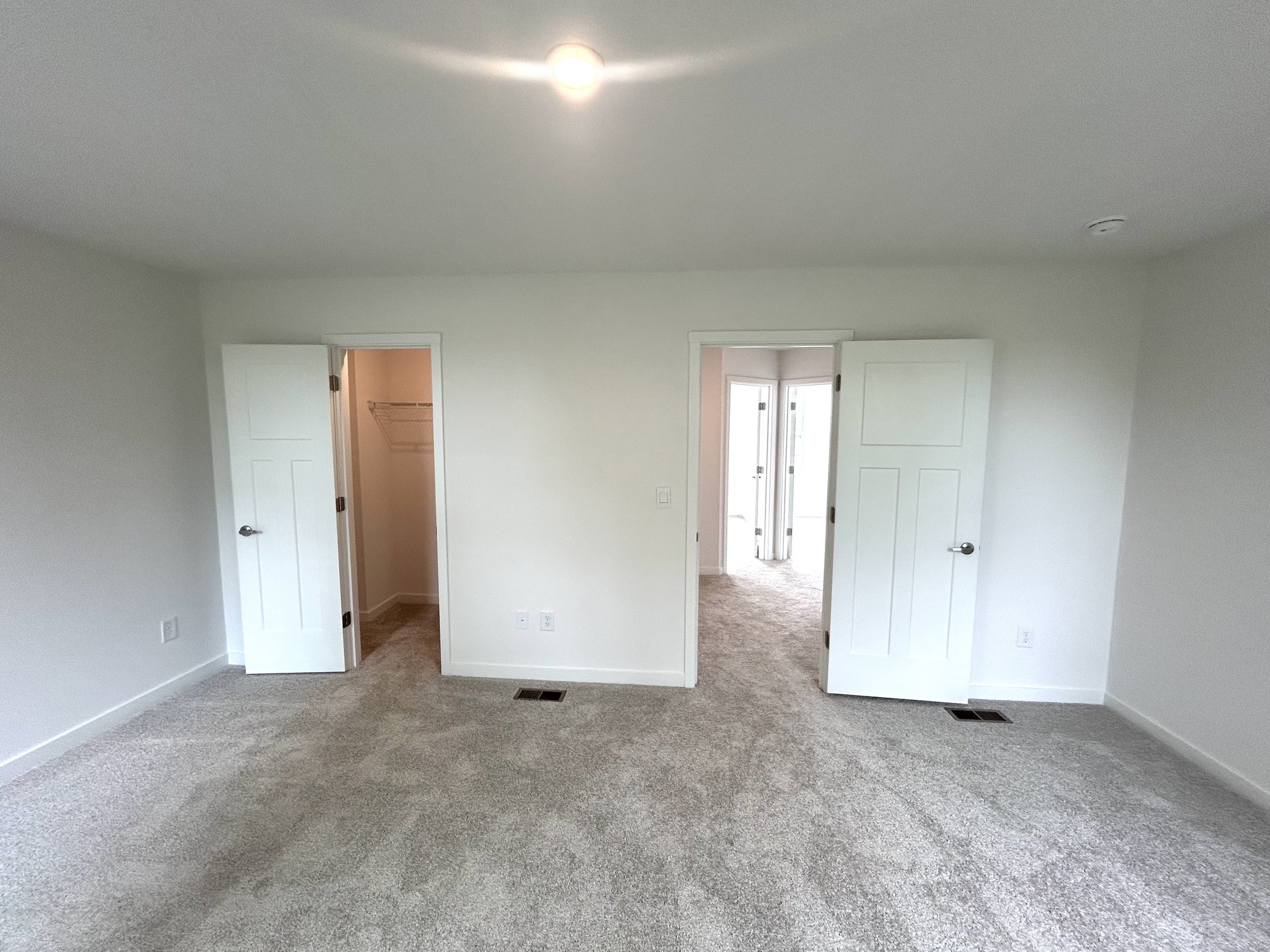 Spacious and modern bedroom interior featuring carpeted flooring and two open doors leading to additional rooms.
