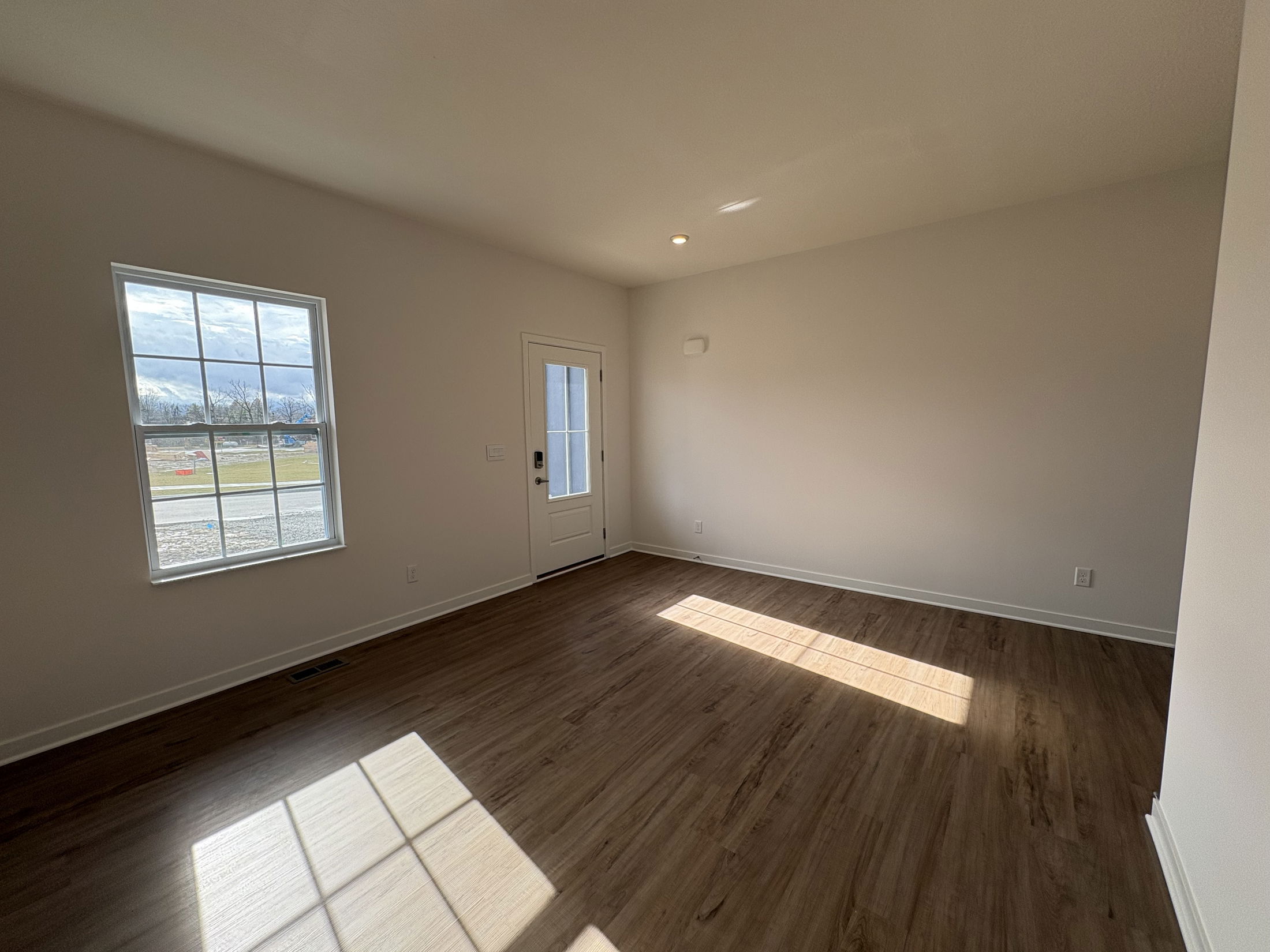 Bright and spacious interior of a modern home featuring a large window and wooden flooring.