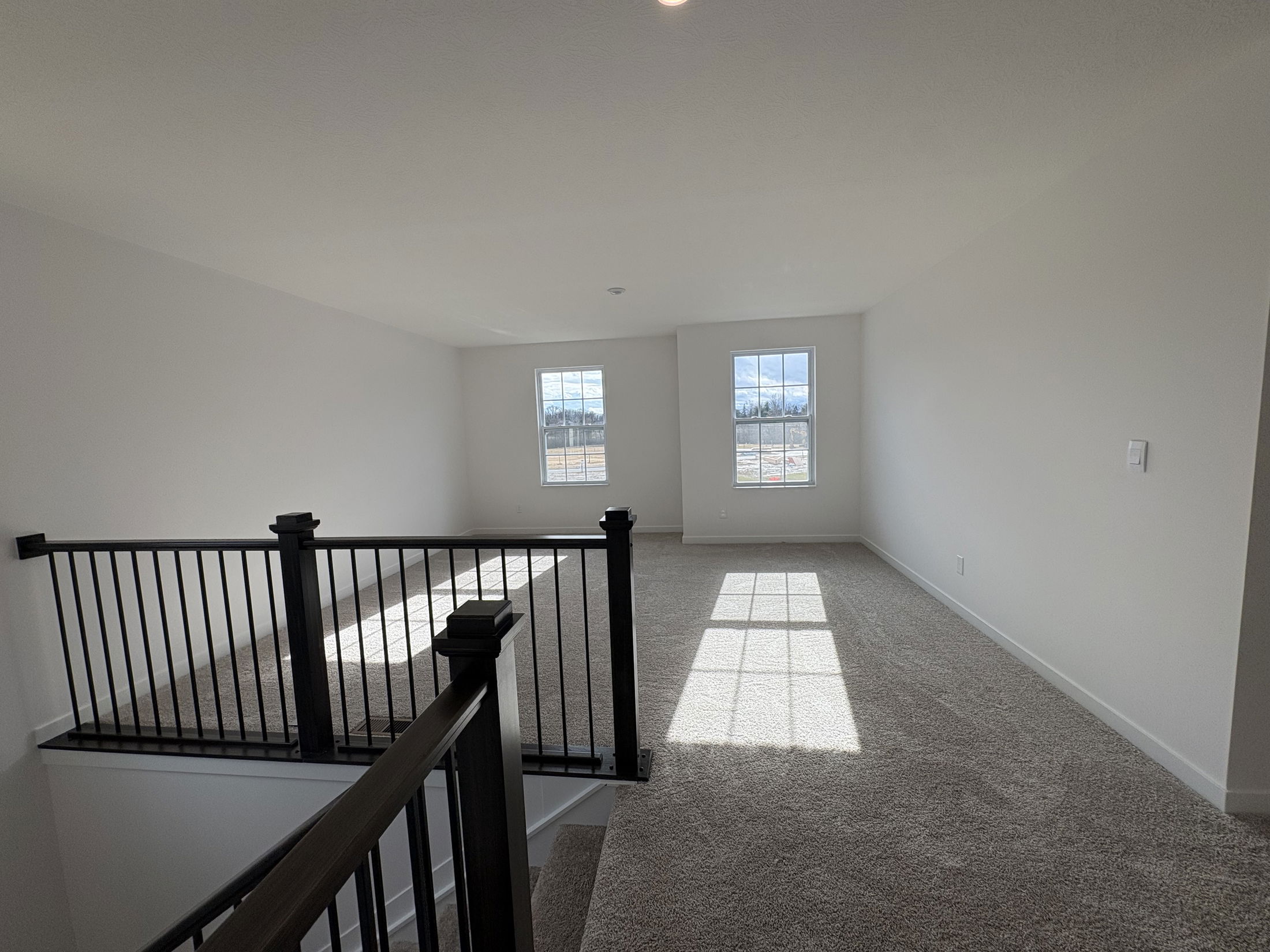 Spacious and bright empty living area with large windows and modern staircase featuring black railings.