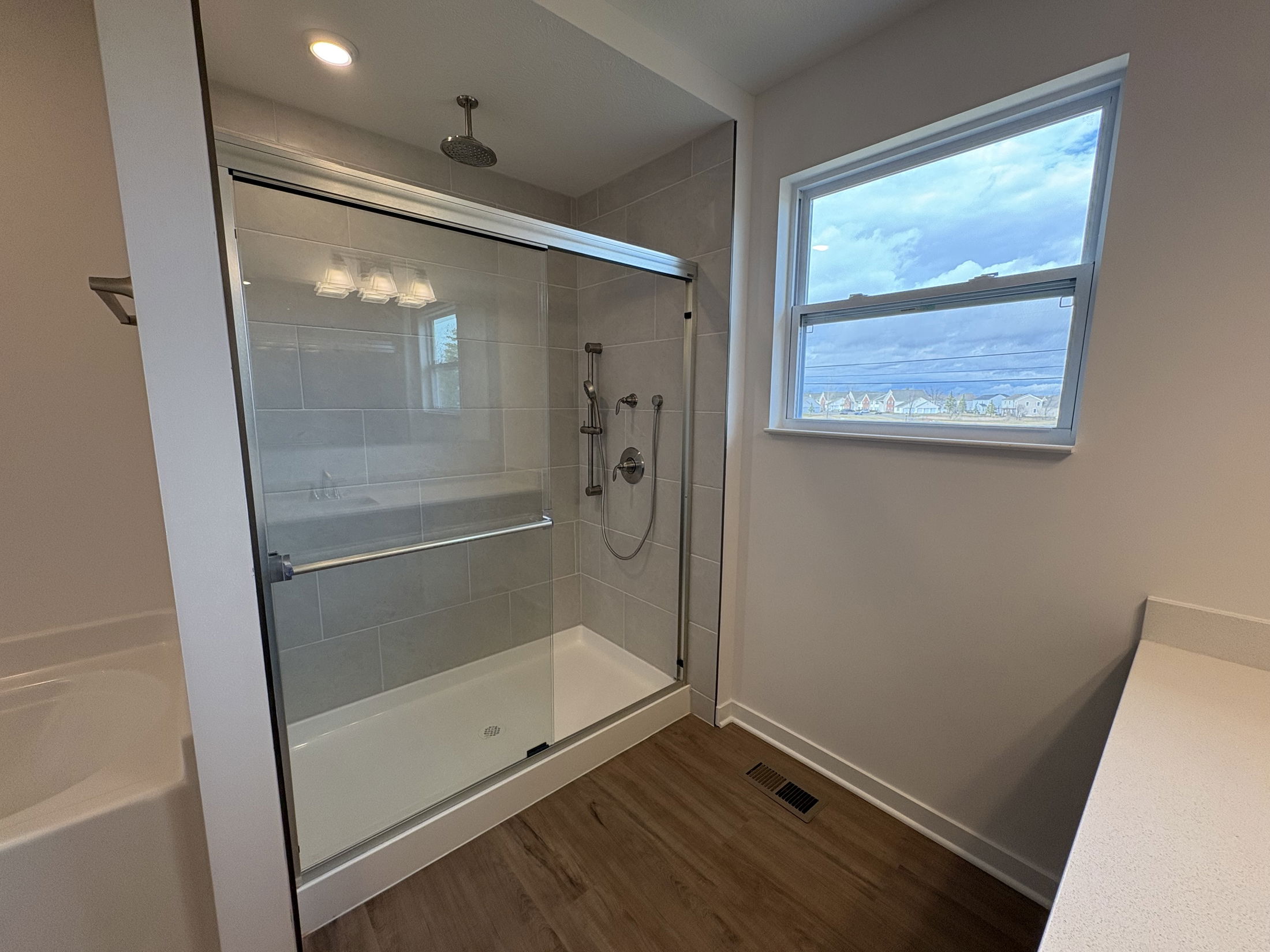 Modern bathroom featuring a glass-enclosed shower, sleek tile walls, and large window with natural light.