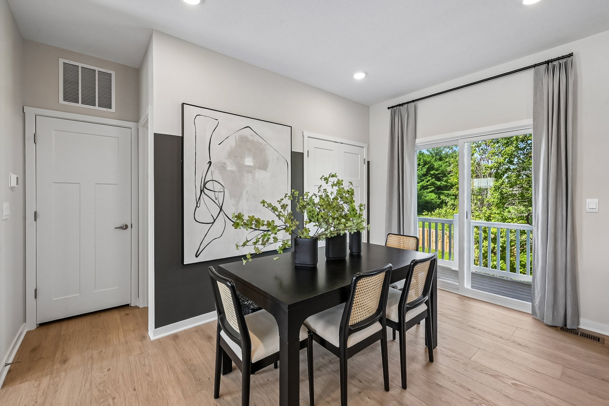 A dining area with a black table and four chairs, featuring a large abstract art piece on the wall and a sliding glass door leading to a deck.