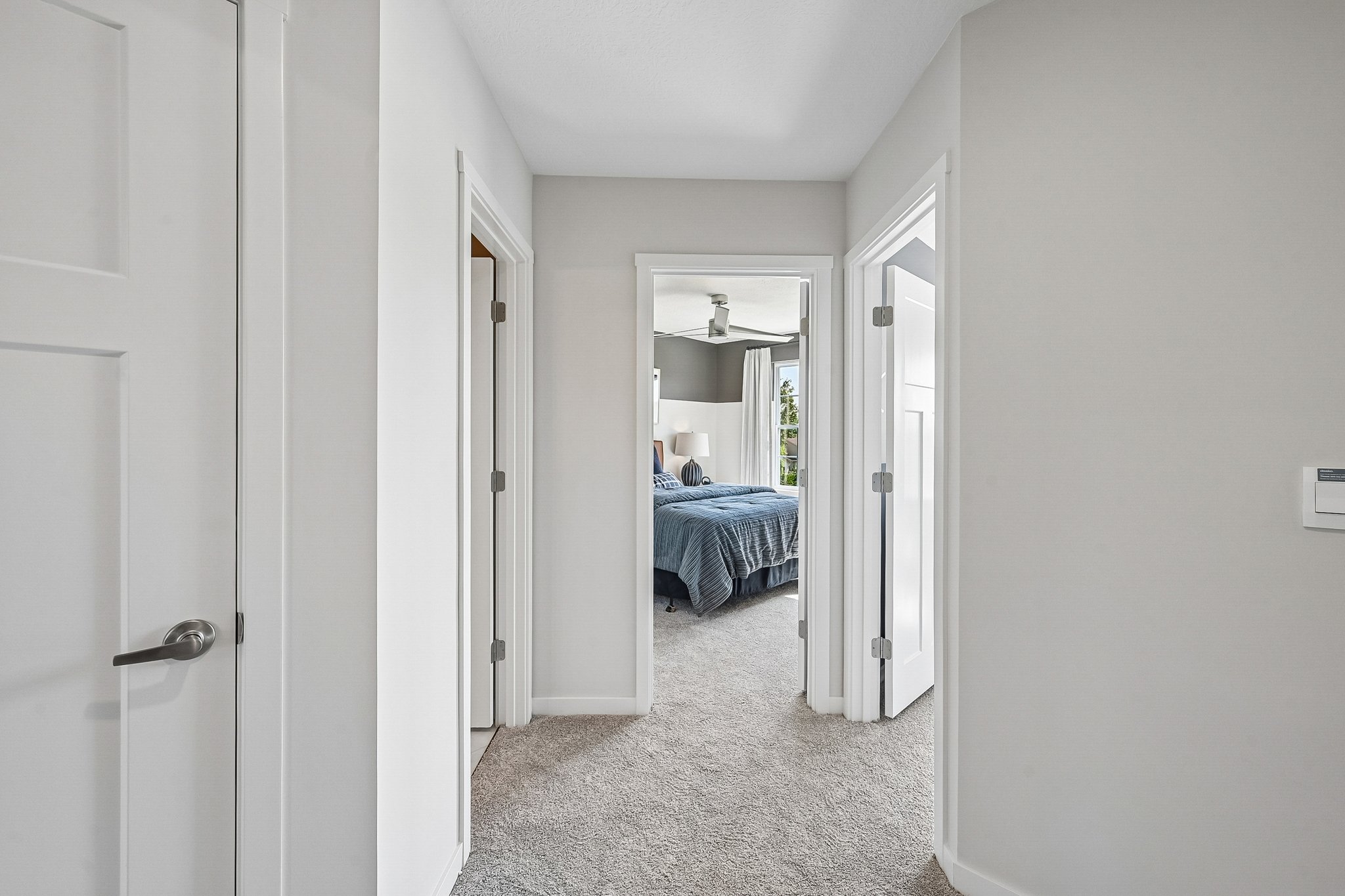 A view of a hallway leading to a bedroom with a ceiling fan and blue bedding.