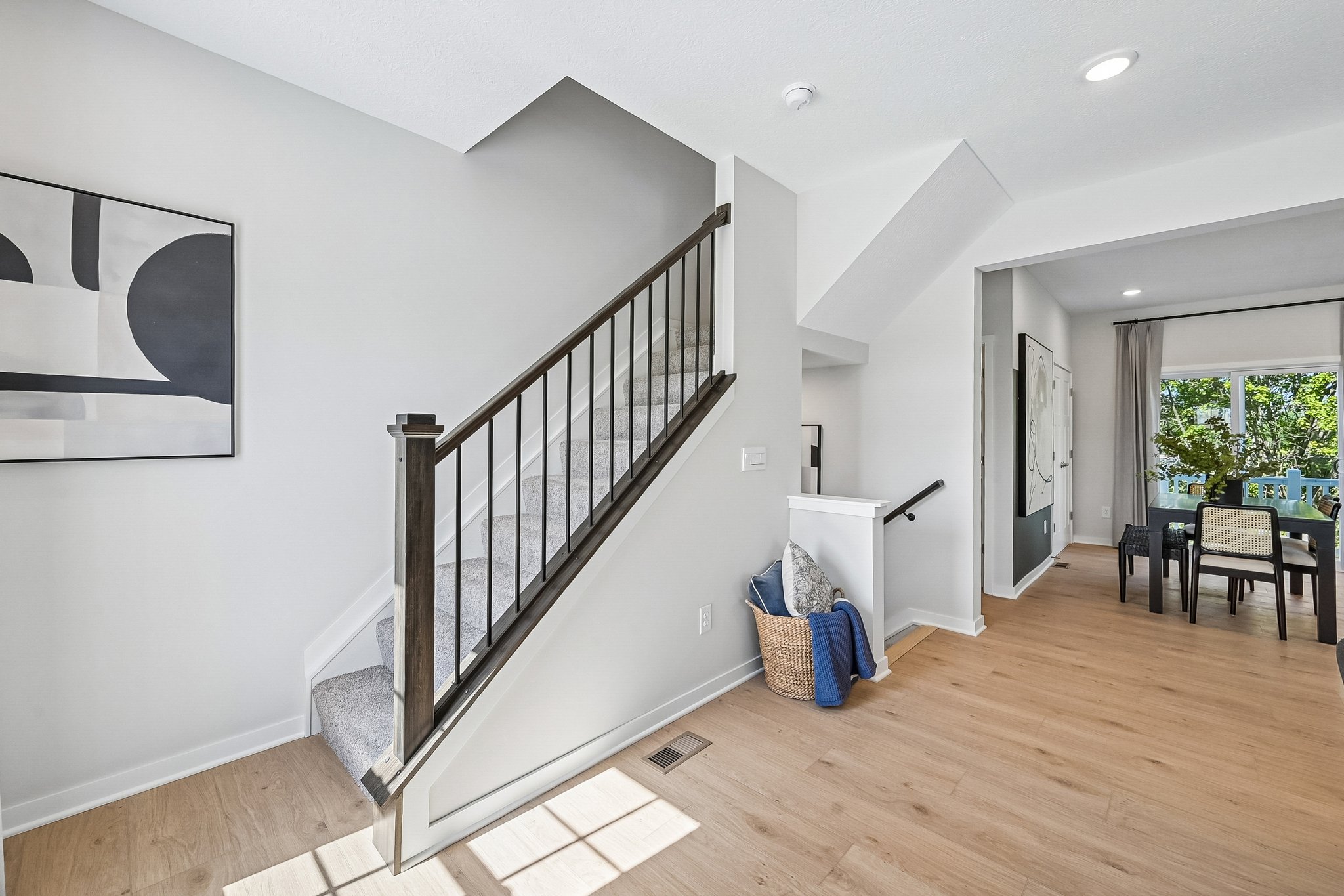 A spacious interior with a staircase, modern artwork on the wall, and a dining area visible through an open doorway.