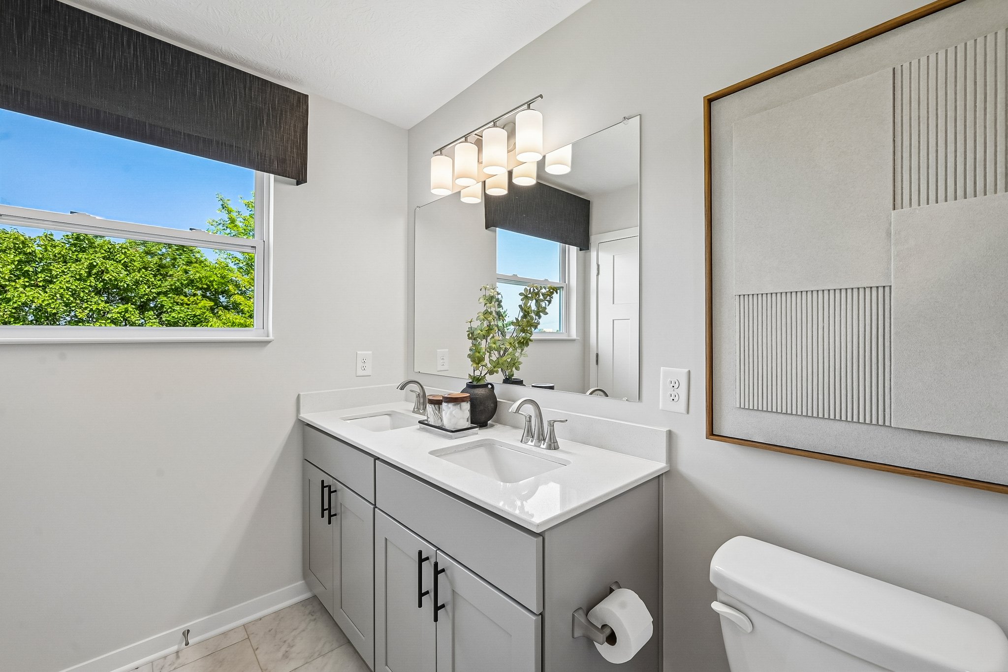 A modern bathroom featuring a double sink vanity, a large mirror, and a window showing greenery outside.