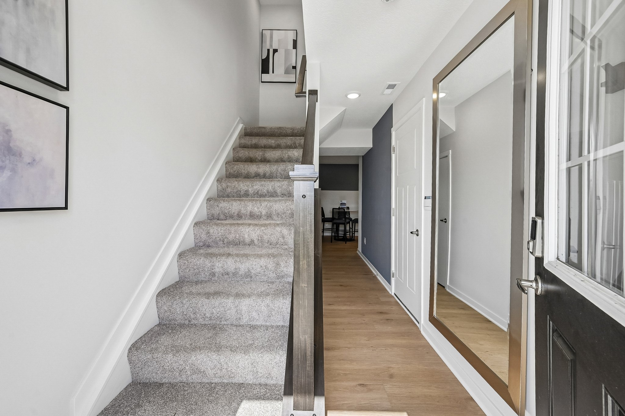 A well-lit entryway features a staircase leading to an upper level, with a door on the right and a dining area visible in the background.