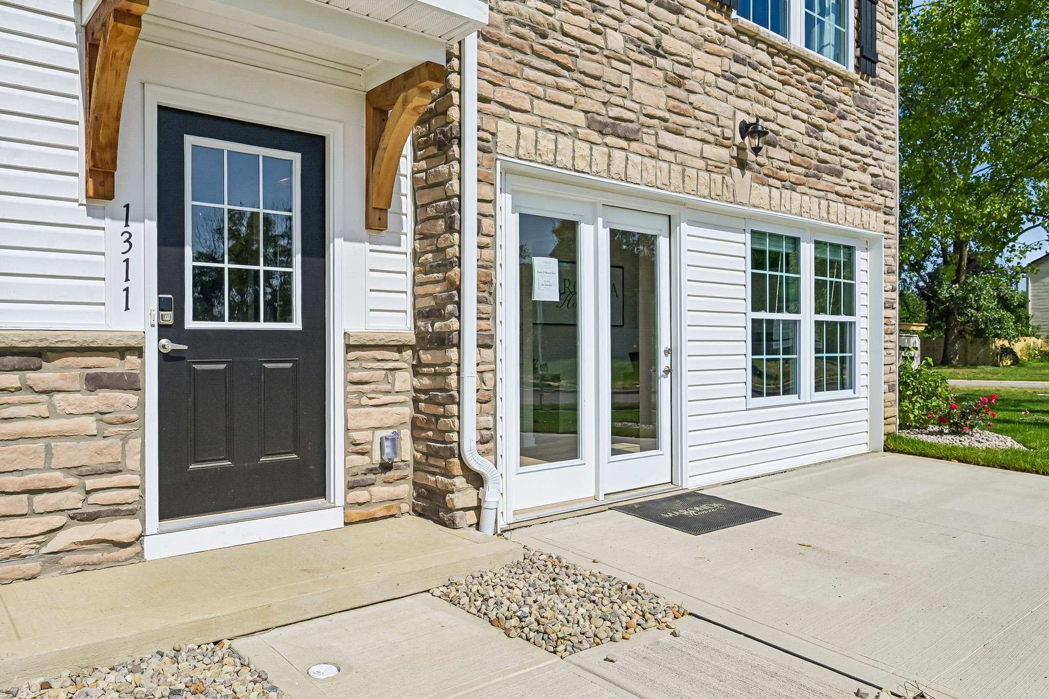A modern residential entrance featuring a dark front door, glass sliding door, and decorative stonework.