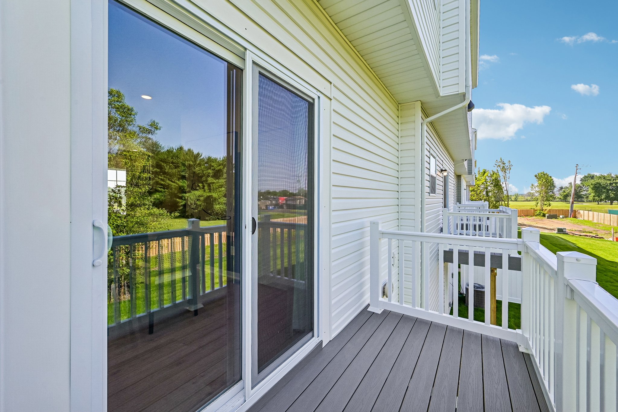 A sliding glass door opens onto a balcony with a white railing, overlooking a green landscape.
