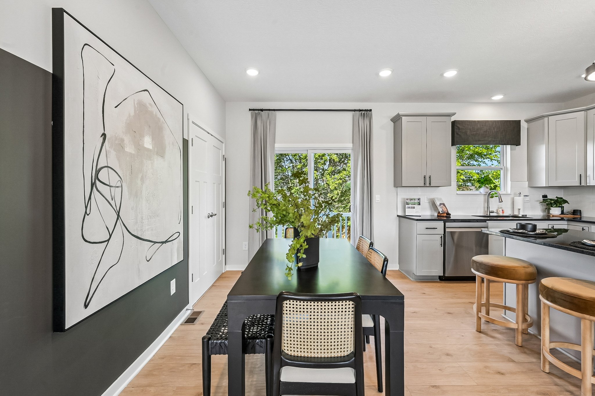 Modern kitchen with a black dining table, wooden bar stools, and a large abstract painting on the wall.