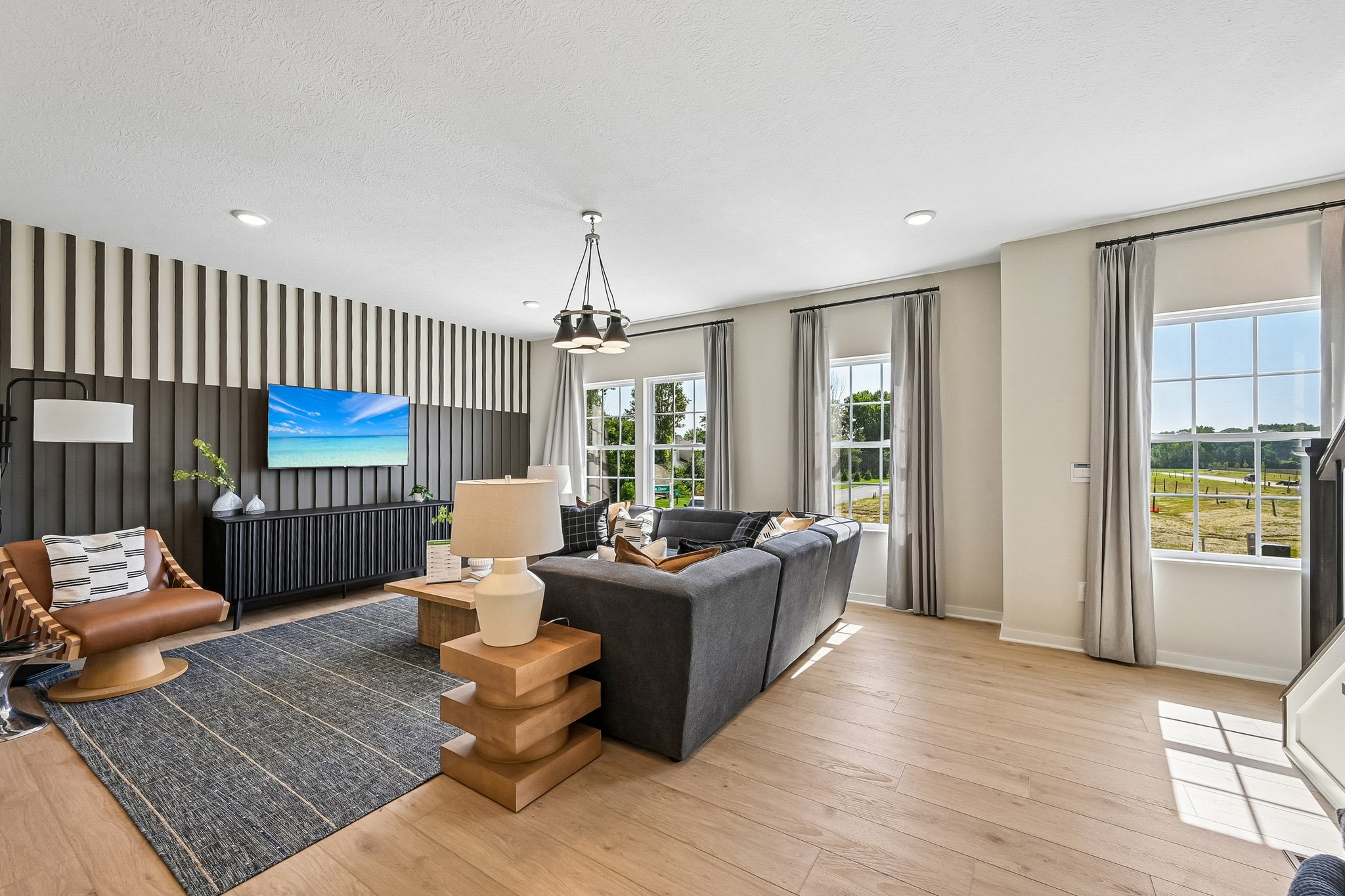 Modern living room with large windows, stylish furniture, and a wall-mounted TV.