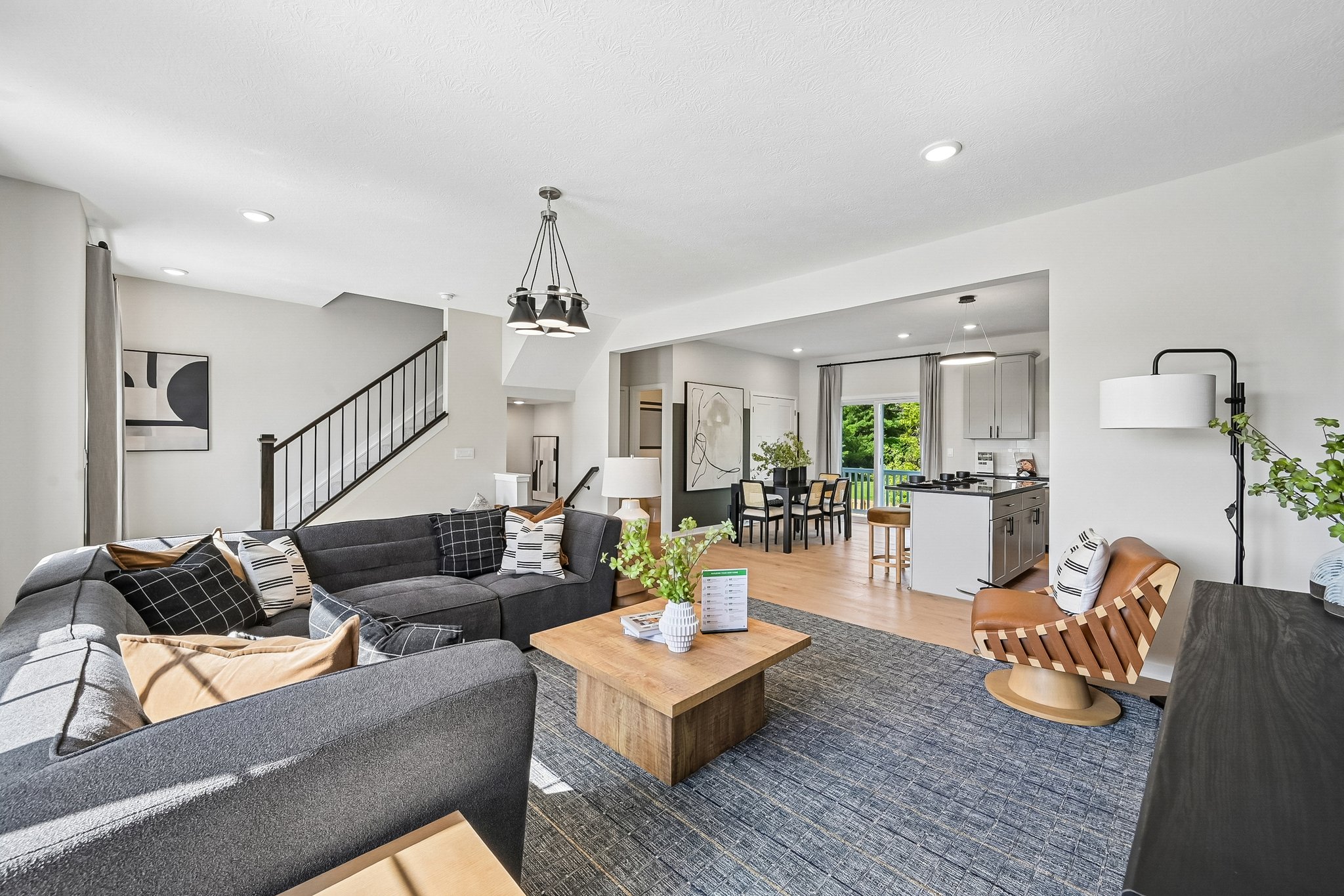 Modern living room featuring a dark sectional sofa, wooden coffee table, and contemporary decor with an open kitchen visible in the background.