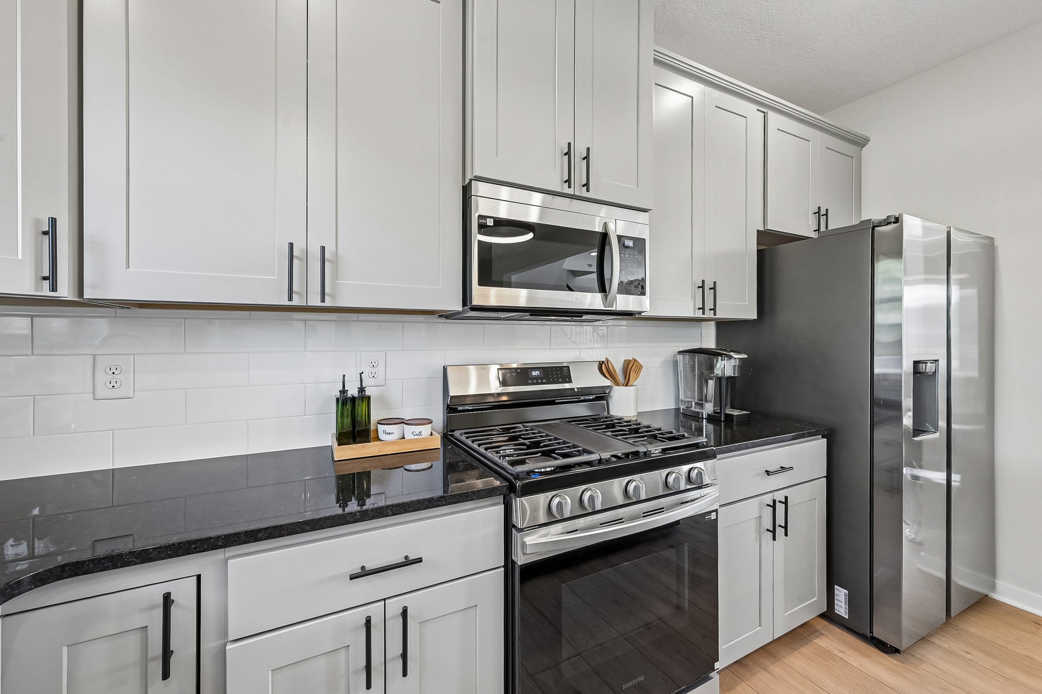 Modern kitchen featuring gray cabinetry, stainless steel appliances, and a black countertop.