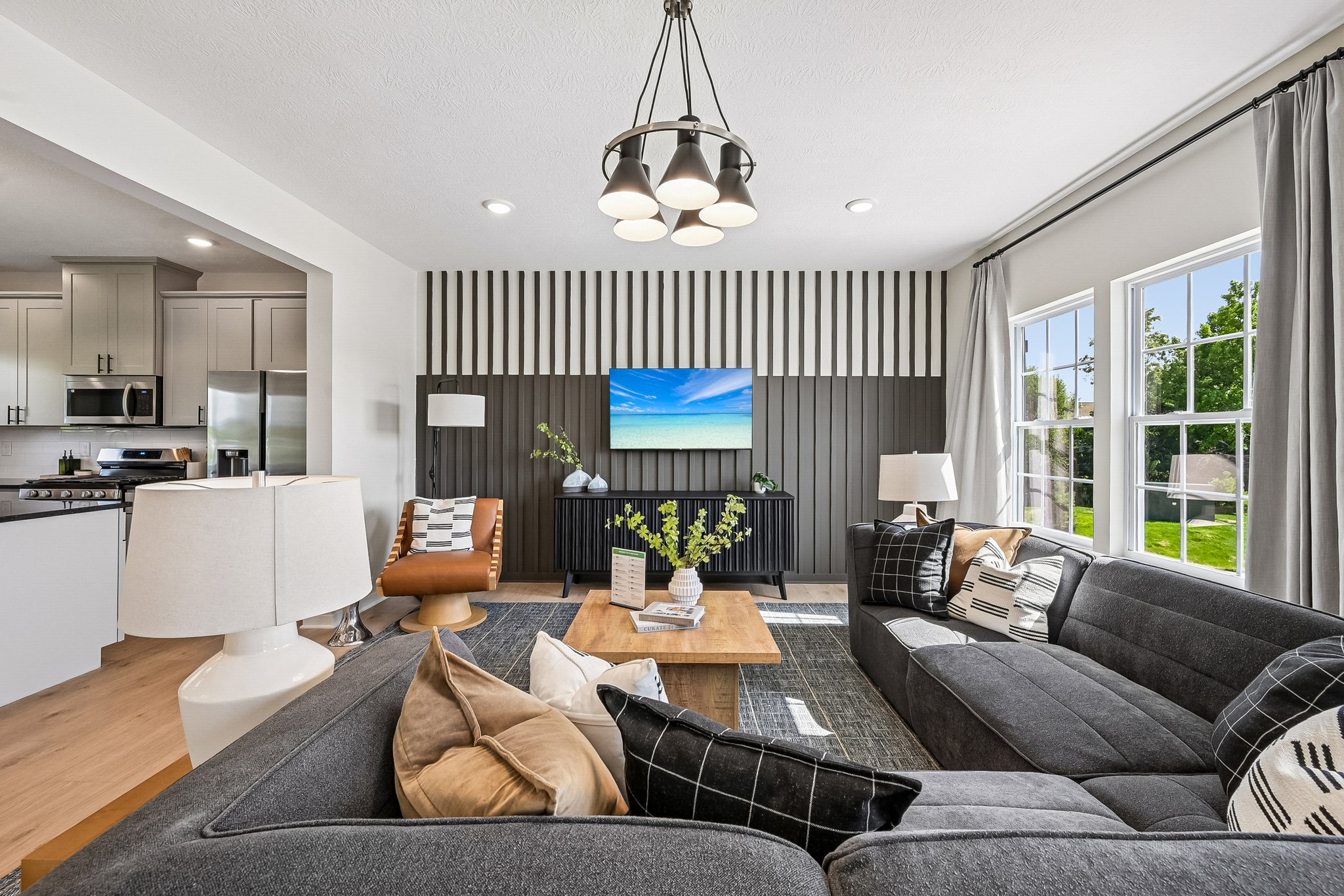 Modern living room with a gray sectional sofa, a wooden coffee table, and a large wall-mounted TV above plants and decorative accessories.