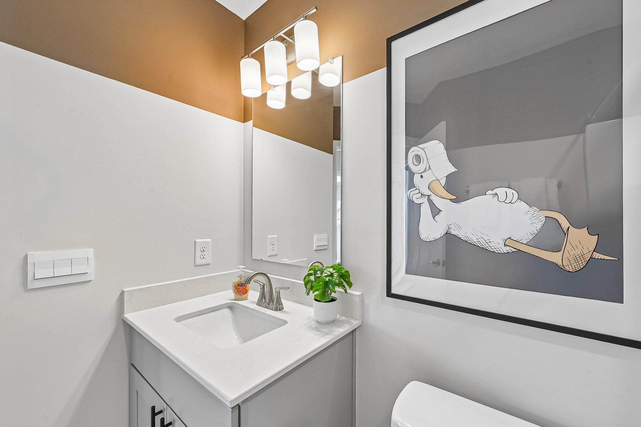A bathroom featuring a white sink, modern lighting, and a framed cartoon artwork on the wall.