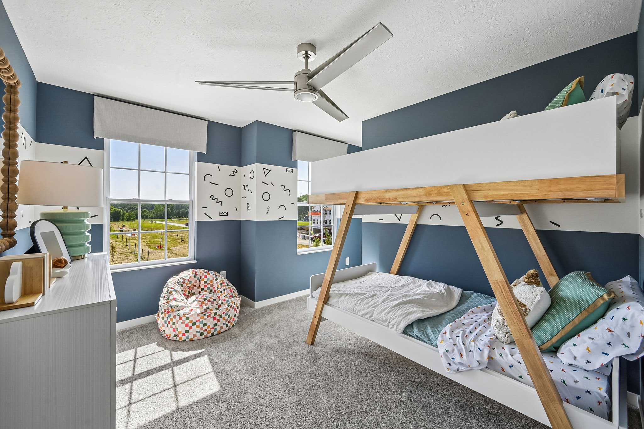 A modern children's bedroom featuring a bunk bed, a colorful bean bag chair, a lamp, and large windows with scenic views.