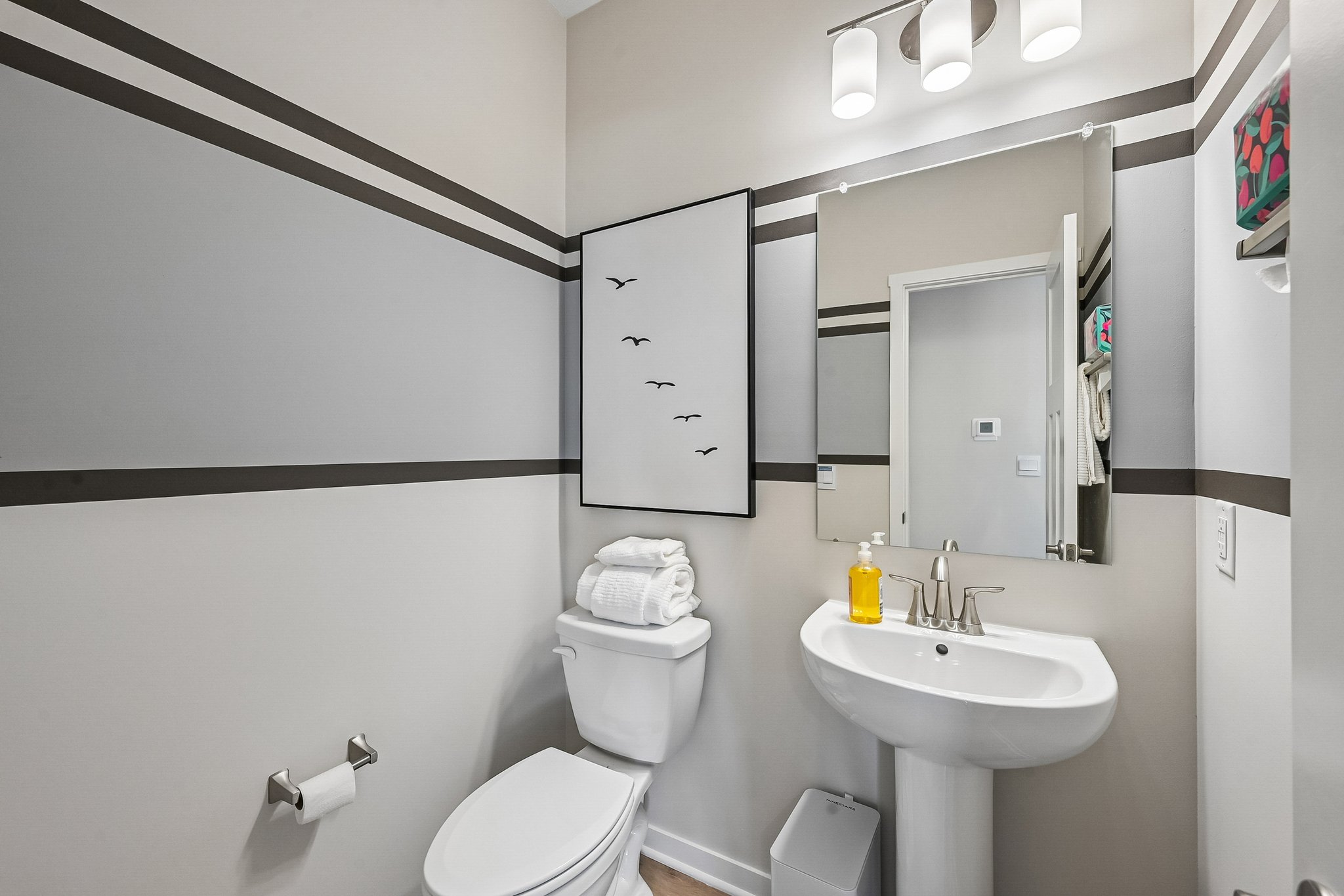 A modern bathroom featuring a white toilet, sink with a mirror, and gray-striped walls adorned with decorative artwork.