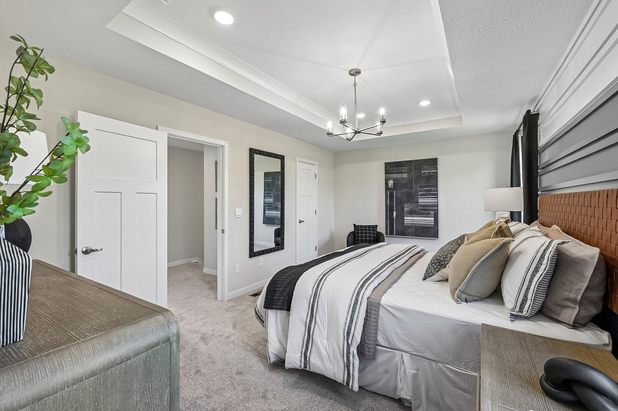 A stylish bedroom featuring a bed with decorative pillows, a chandelier, and a neutral color palette.