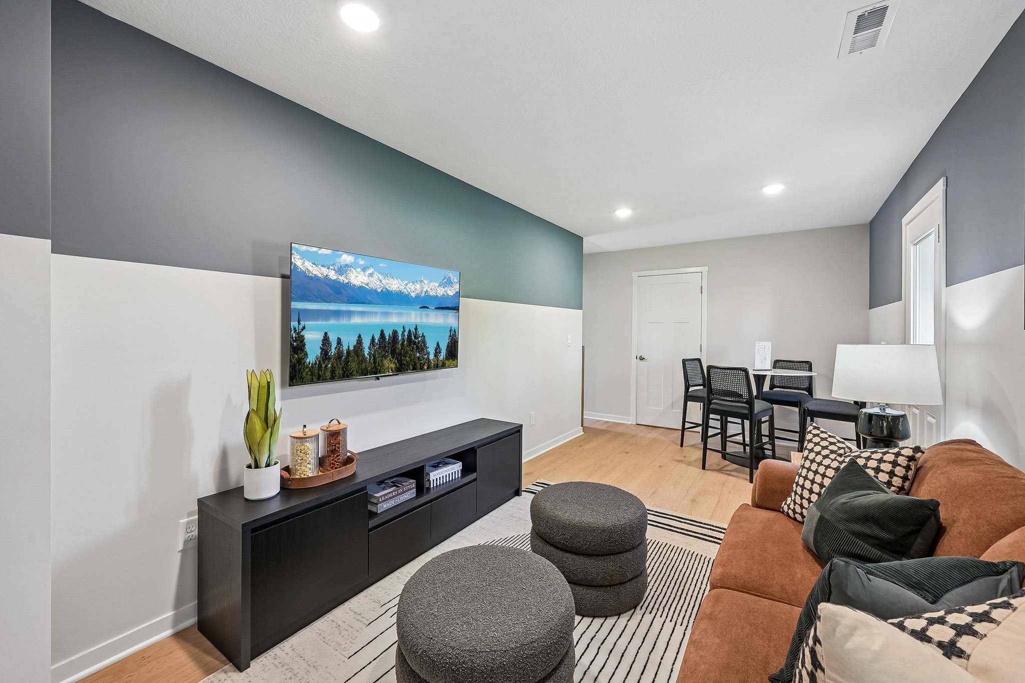 Living room featuring a brown sofa, a black media console with a landscape TV display, and a dining area in the background.
