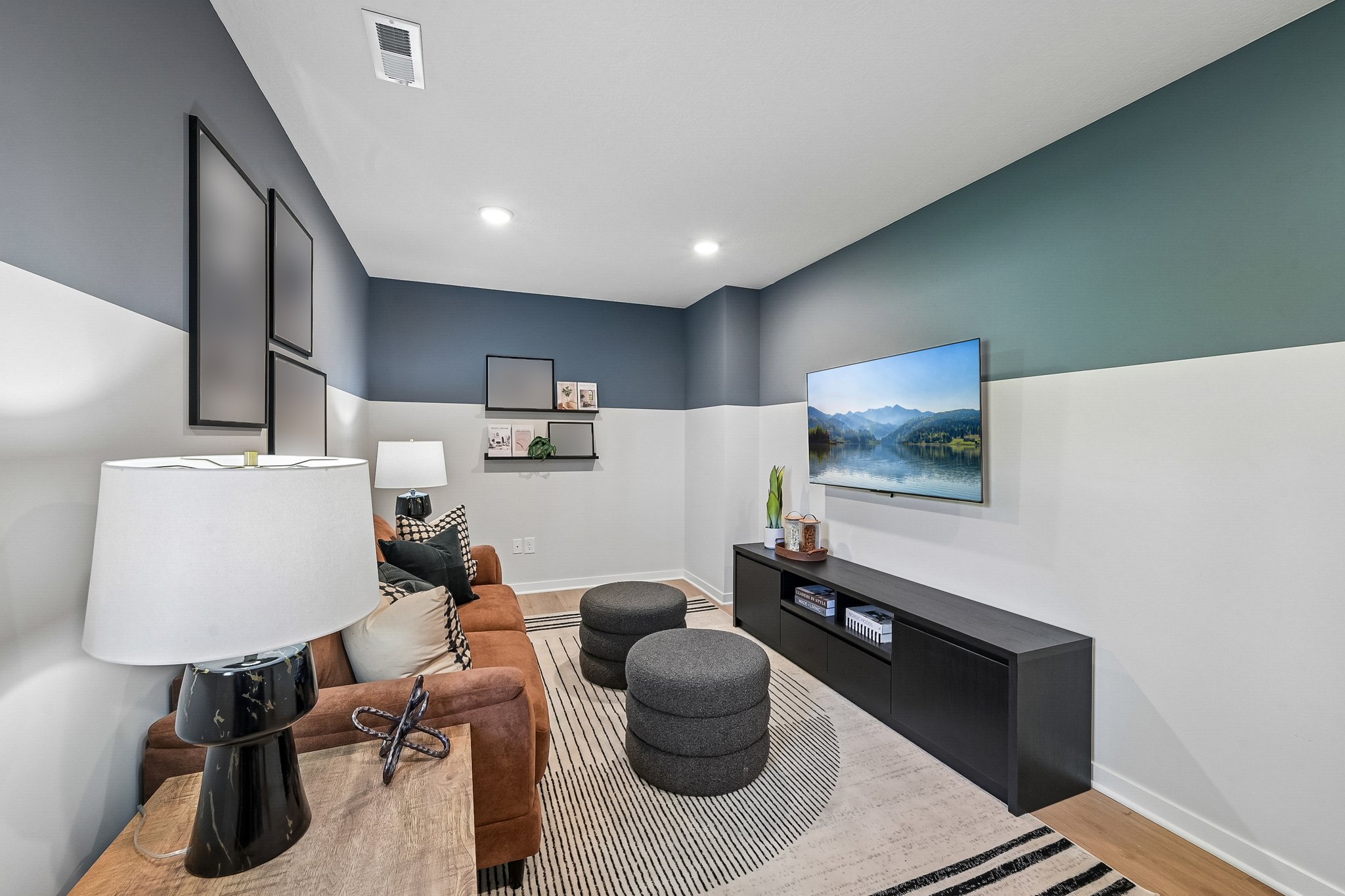 Modern living room featuring a brown sofa, round ottomans, a television mounted on the wall, and decorative shelves.