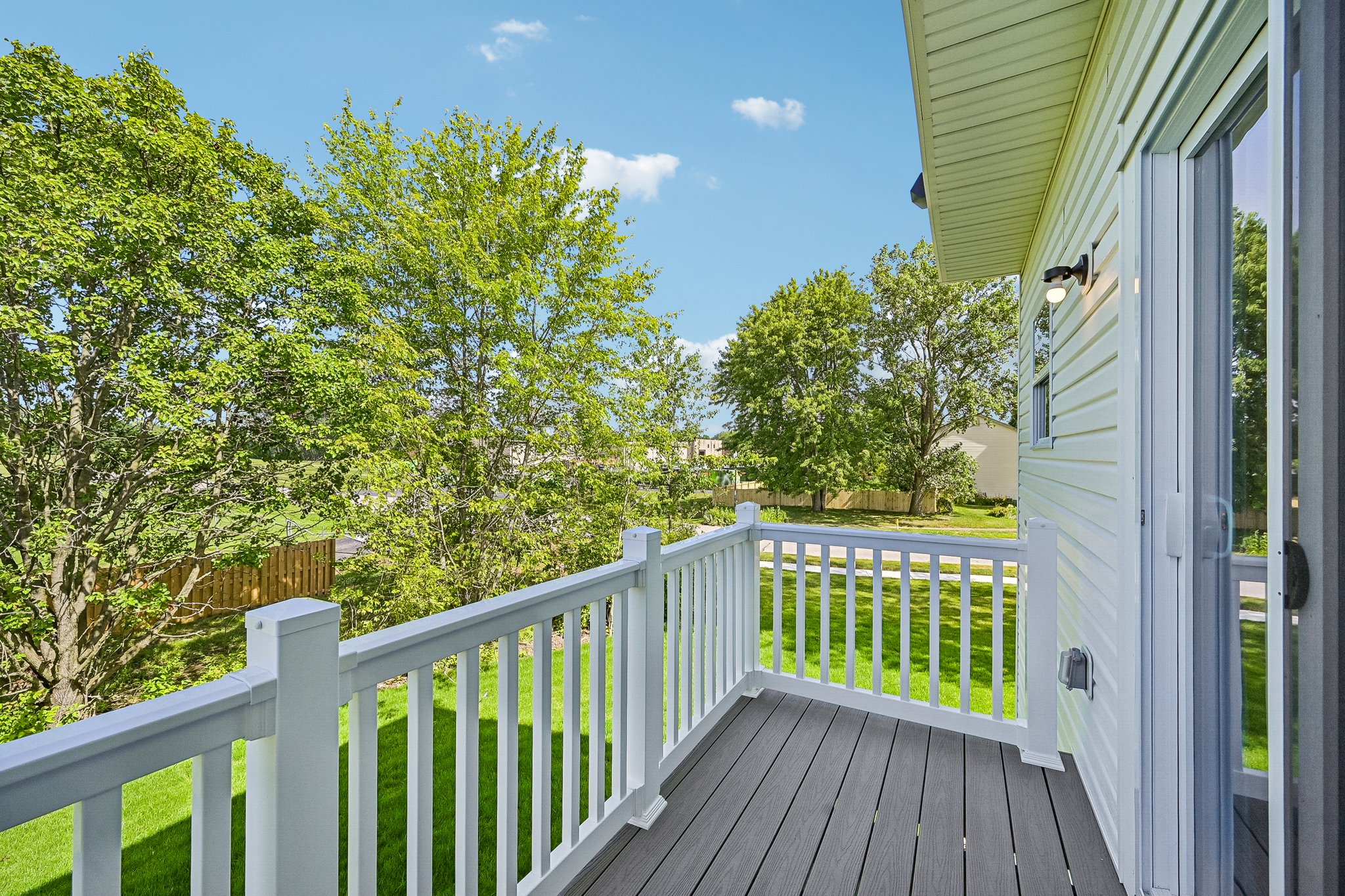 A view from a balcony overlooking a green yard and trees under a blue sky.
