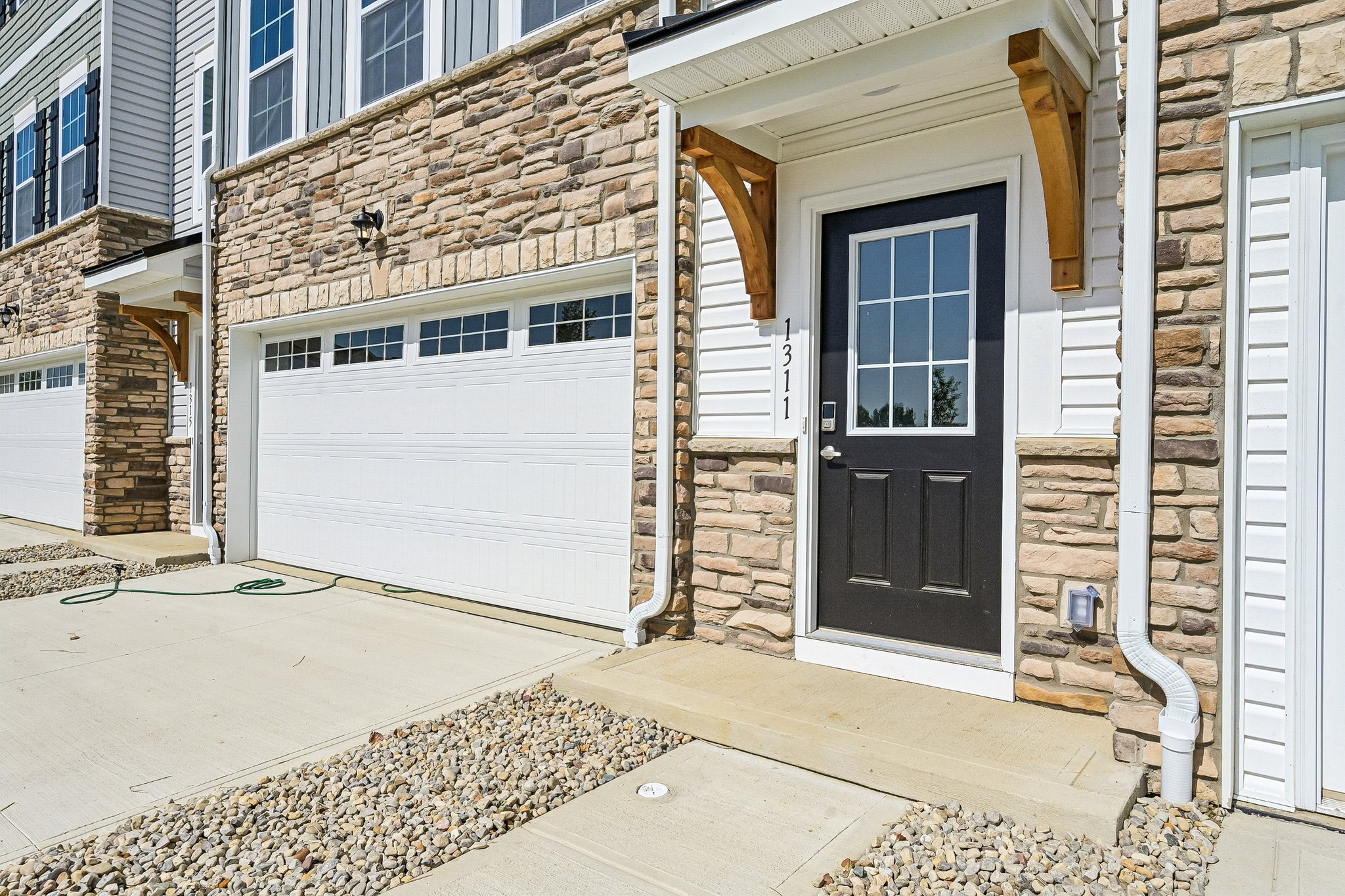 Front entrance of a house featuring a black door and stone facade, with a garage door visible to the left.