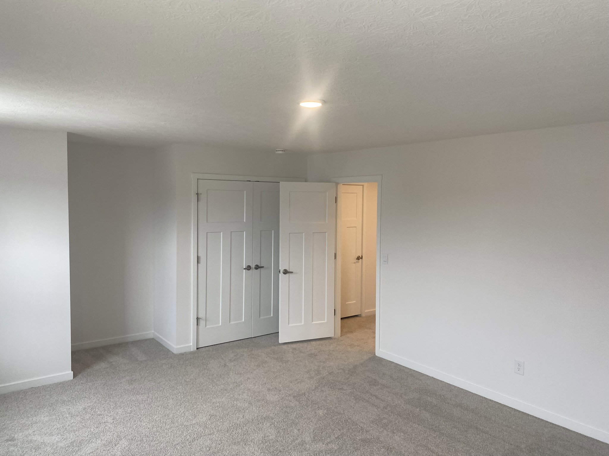 A spacious, empty room with beige carpet and two open doors leading to adjacent areas.