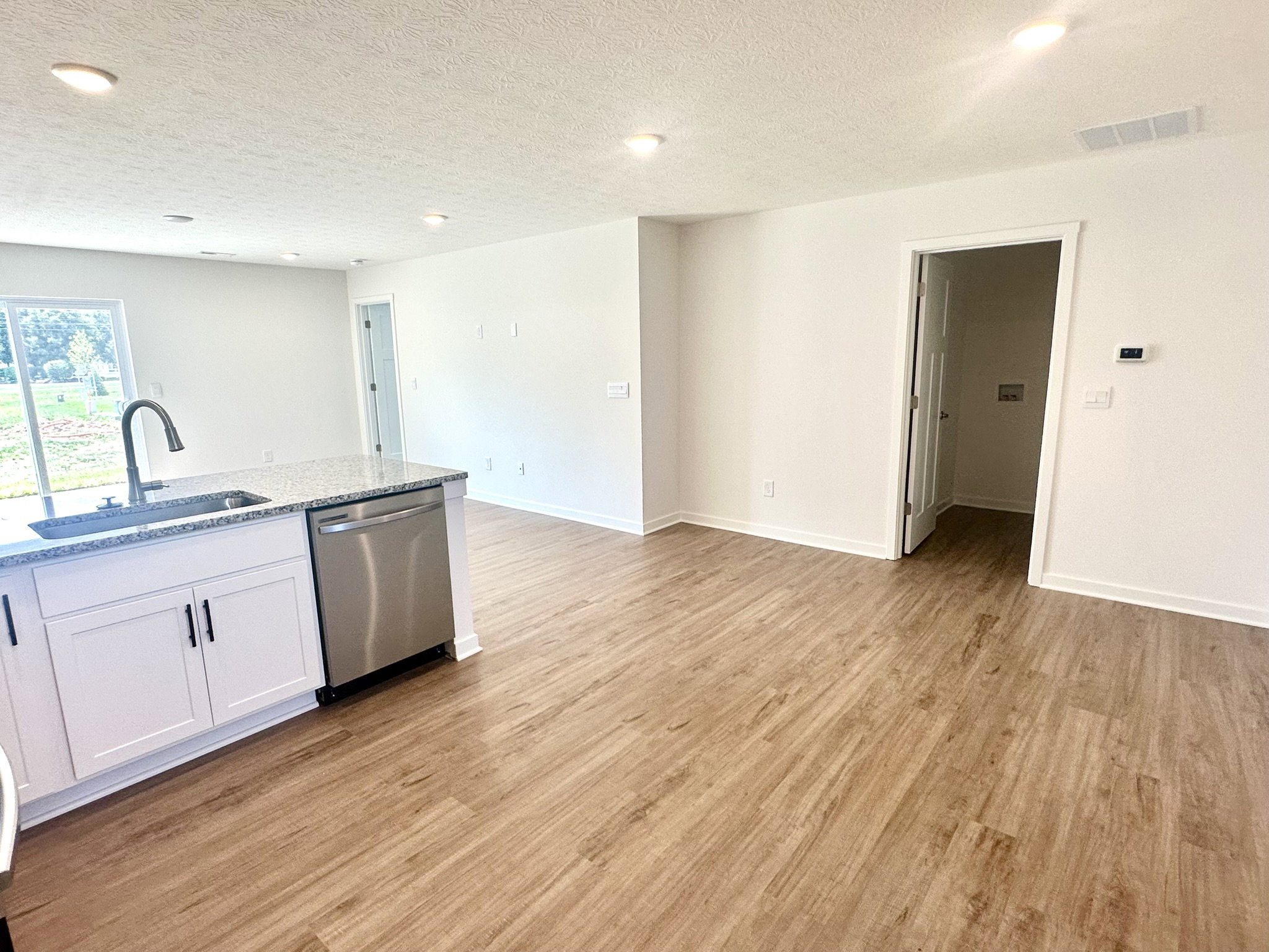 Bright, modern living space with a kitchen, laminate flooring, and a doorway leading to another room.