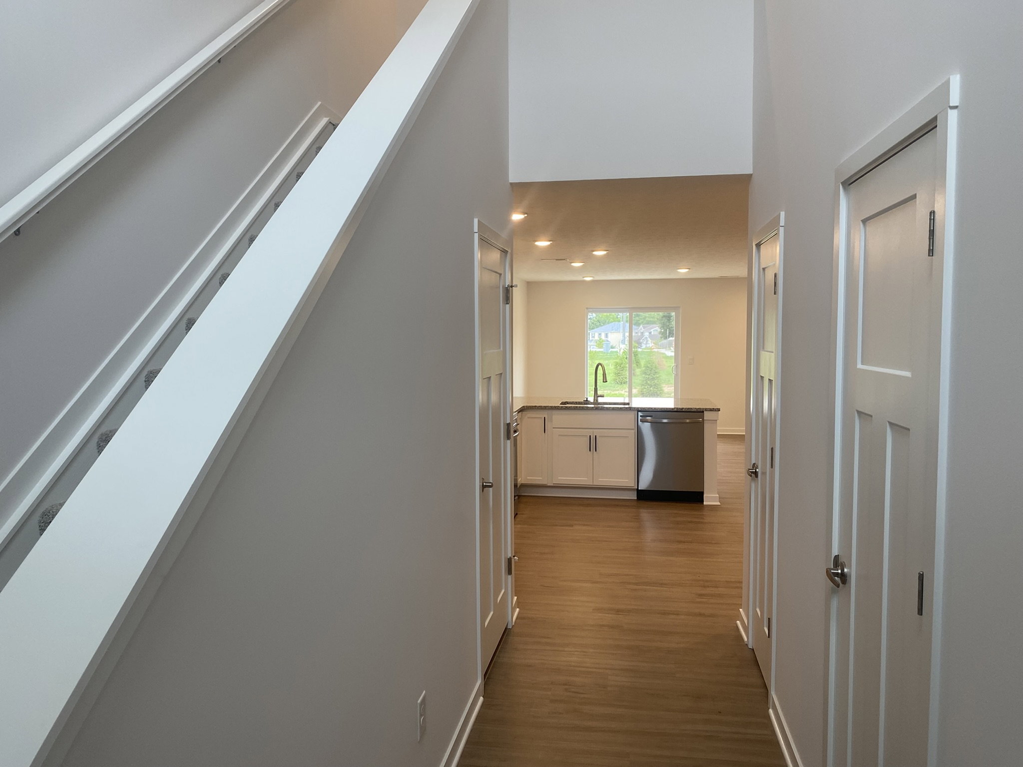 A modern hallway leading to an open kitchen with a view of a green area outside.