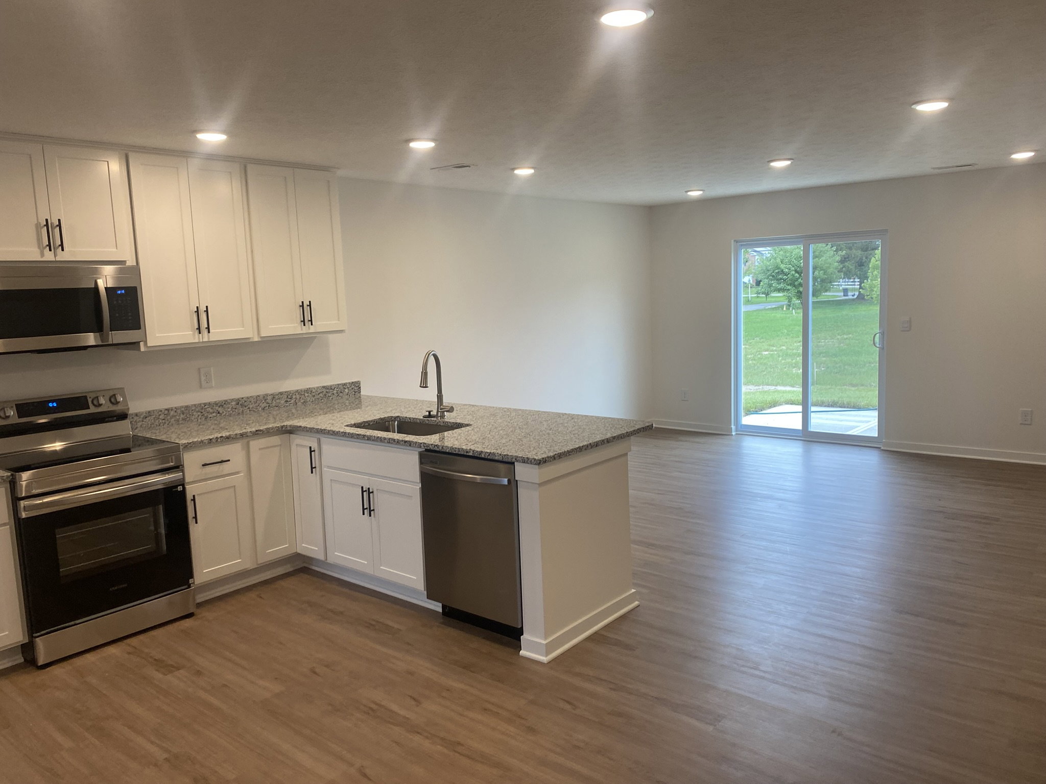 Modern kitchen with stainless steel appliances and a large island, leading into a spacious living area with sliding glass doors to an outdoor space.