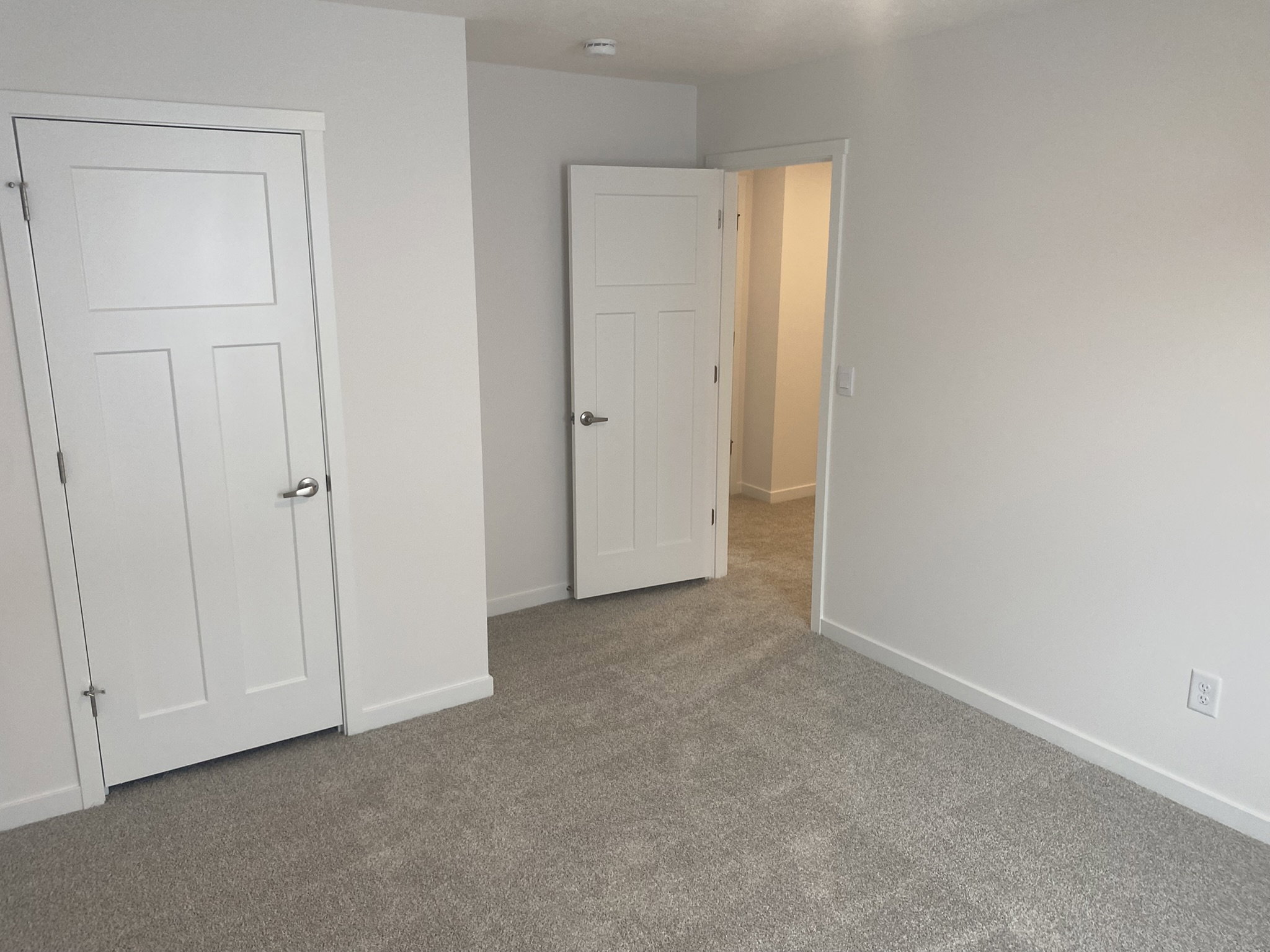 A lightly colored room with two white doors and carpeted flooring.