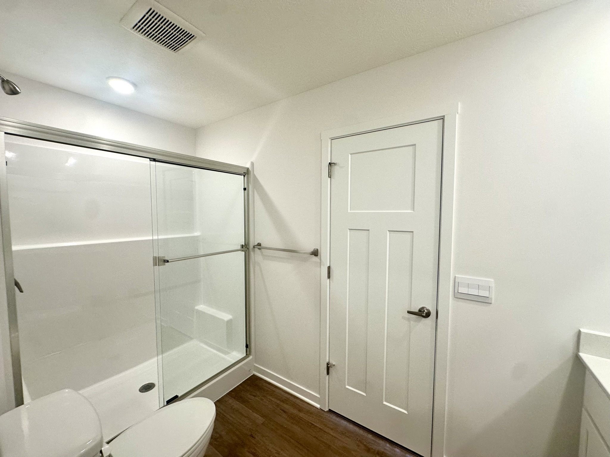 Modern bathroom featuring a glass shower enclosure, white walls, and a doorway.