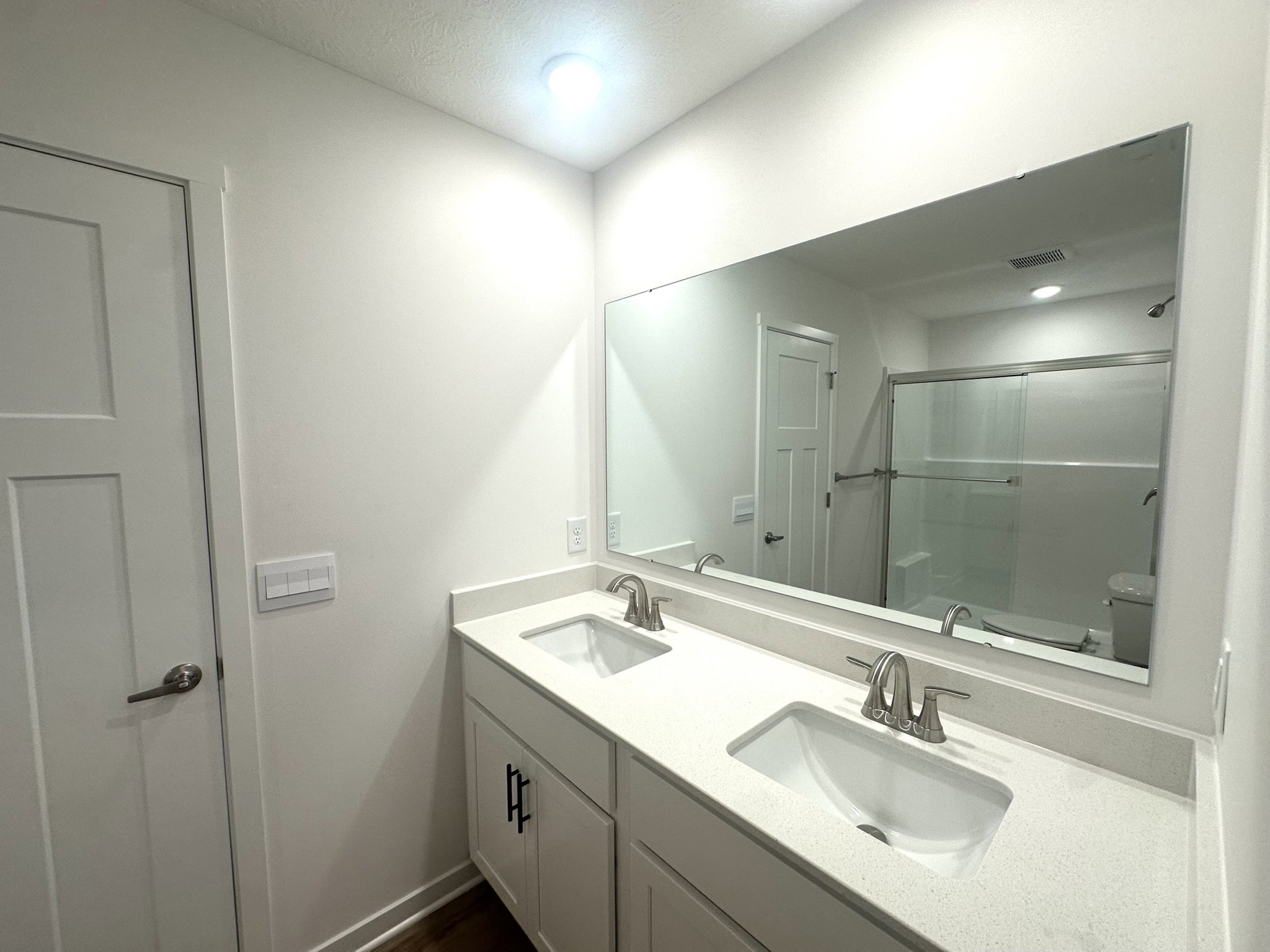 Modern bathroom featuring a double sink vanity with a large mirror, light fixtures, and a sliding glass shower door.