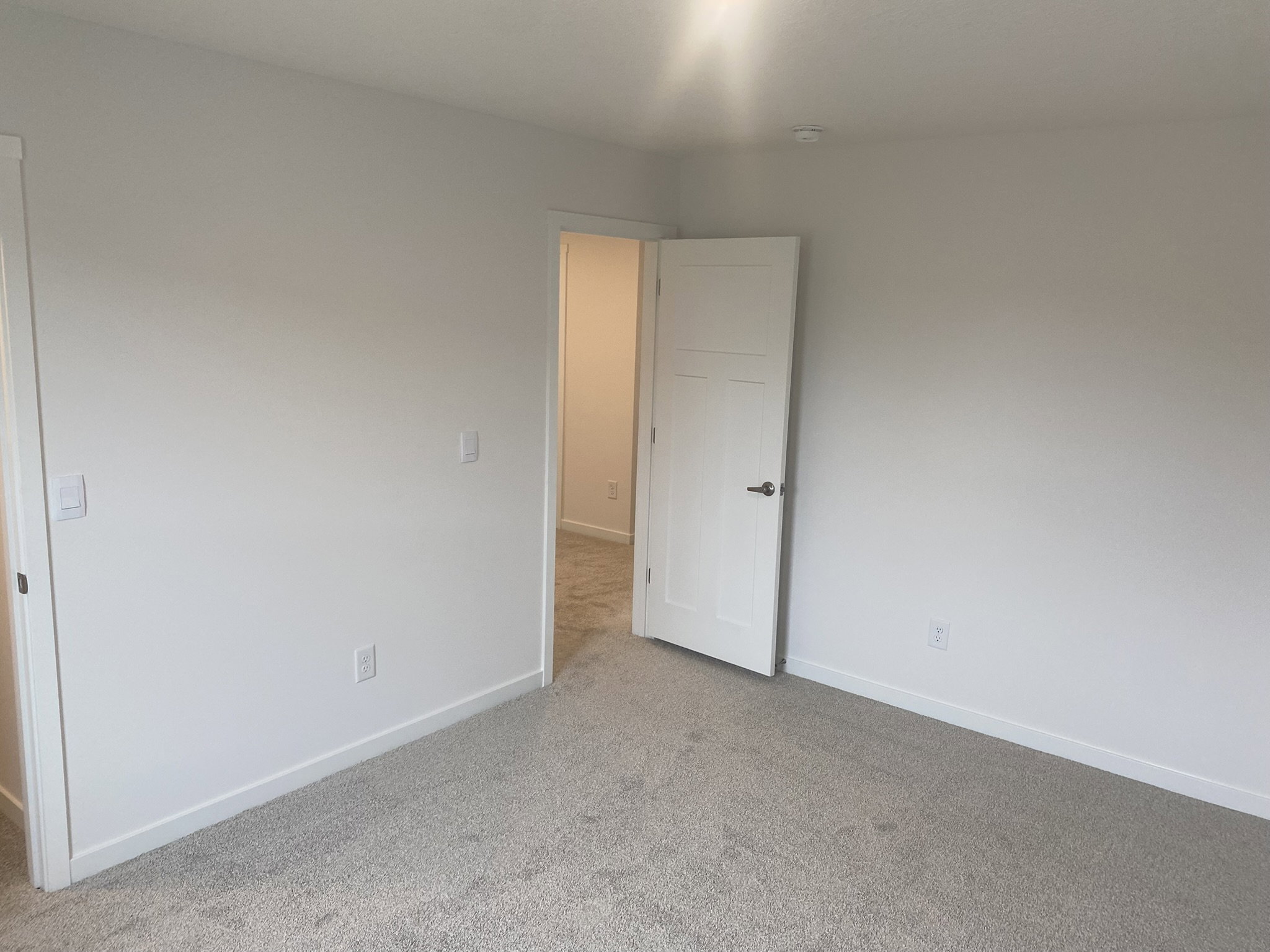 A light, empty room with gray carpet and an open door leading to another space.