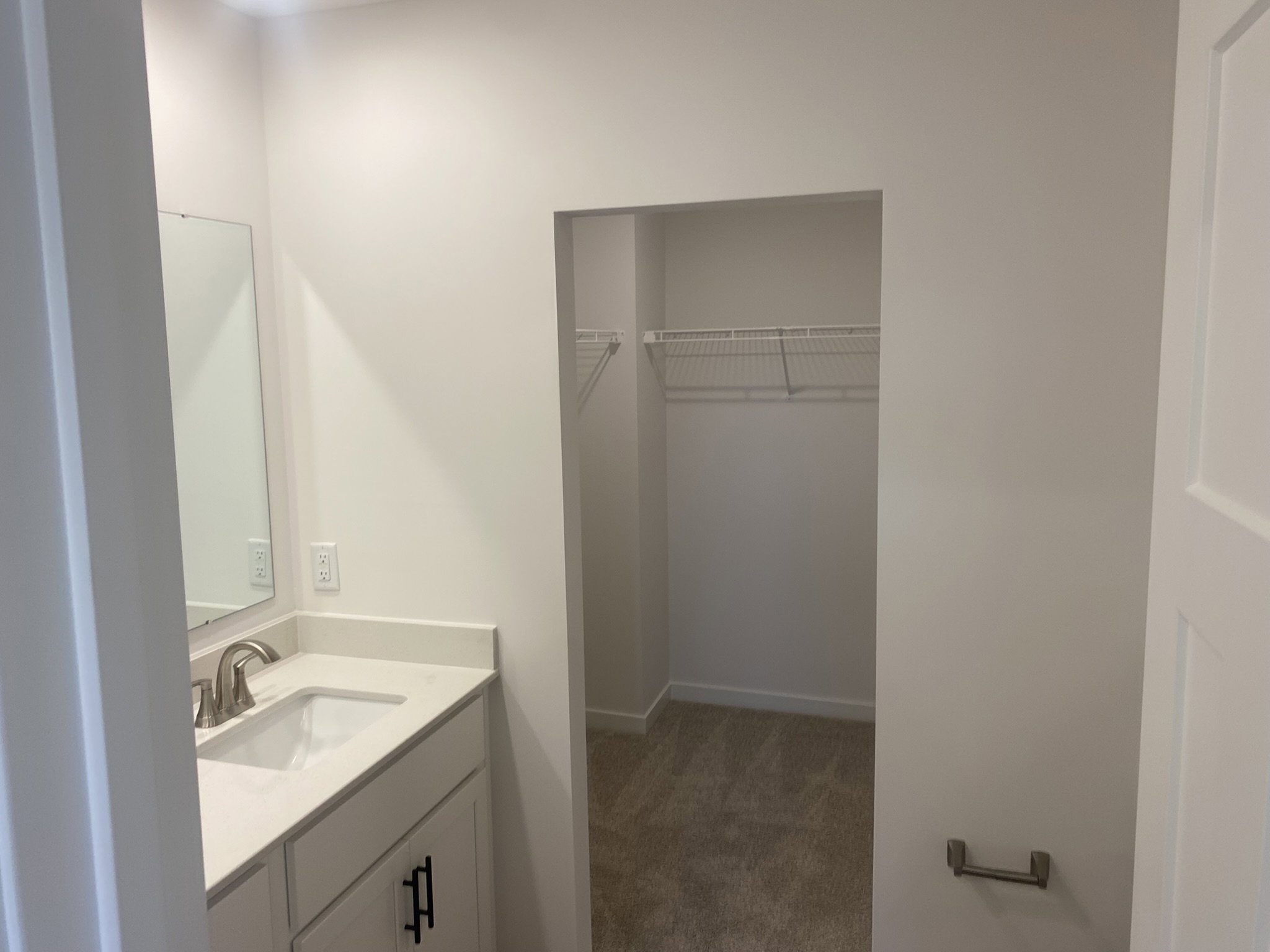A bright, neutral-colored bathroom featuring a sink, mirror, and a closet with wire shelving.