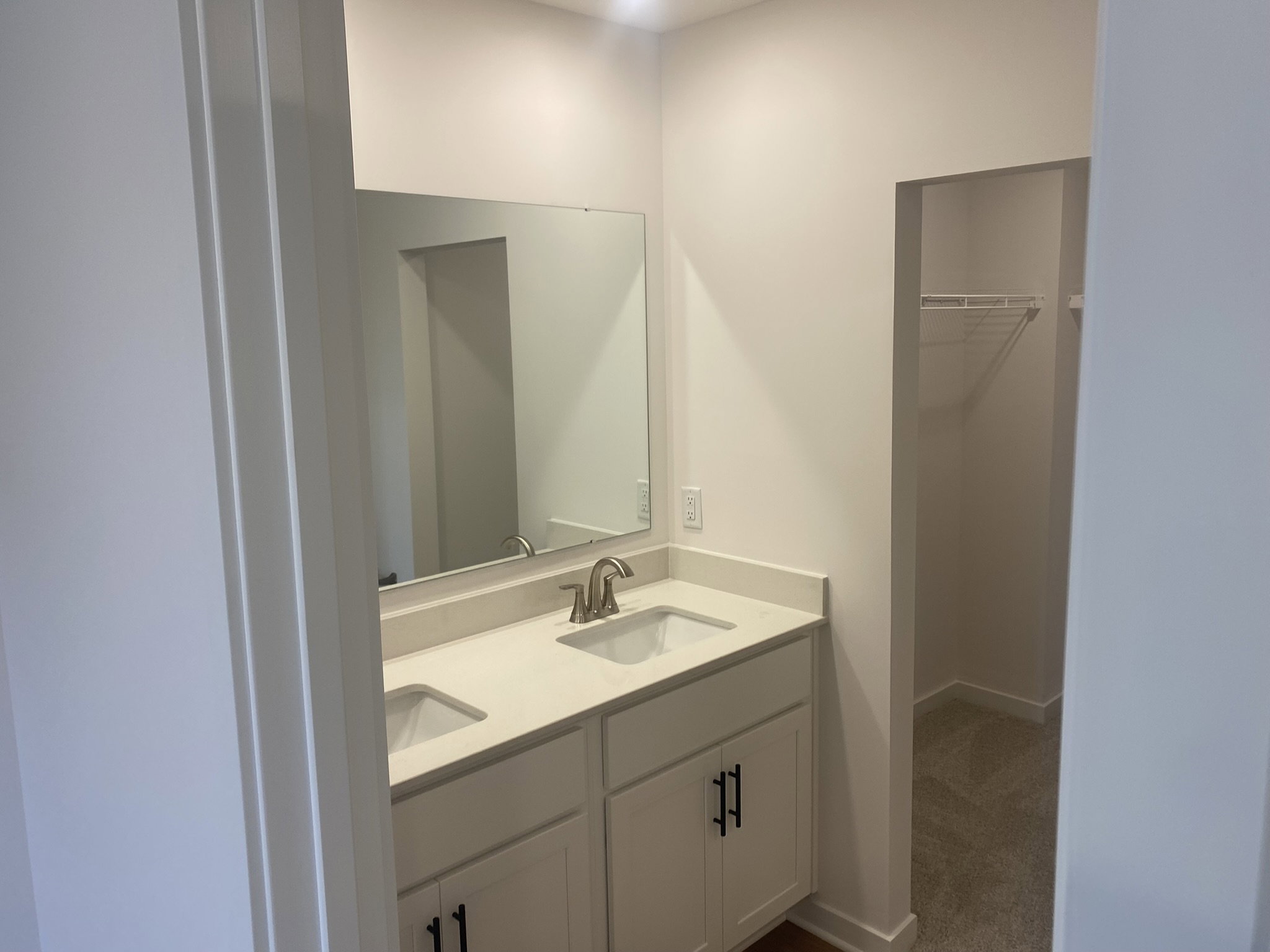 A modern bathroom featuring a double vanity with a large mirror and a closet nook in the corner.