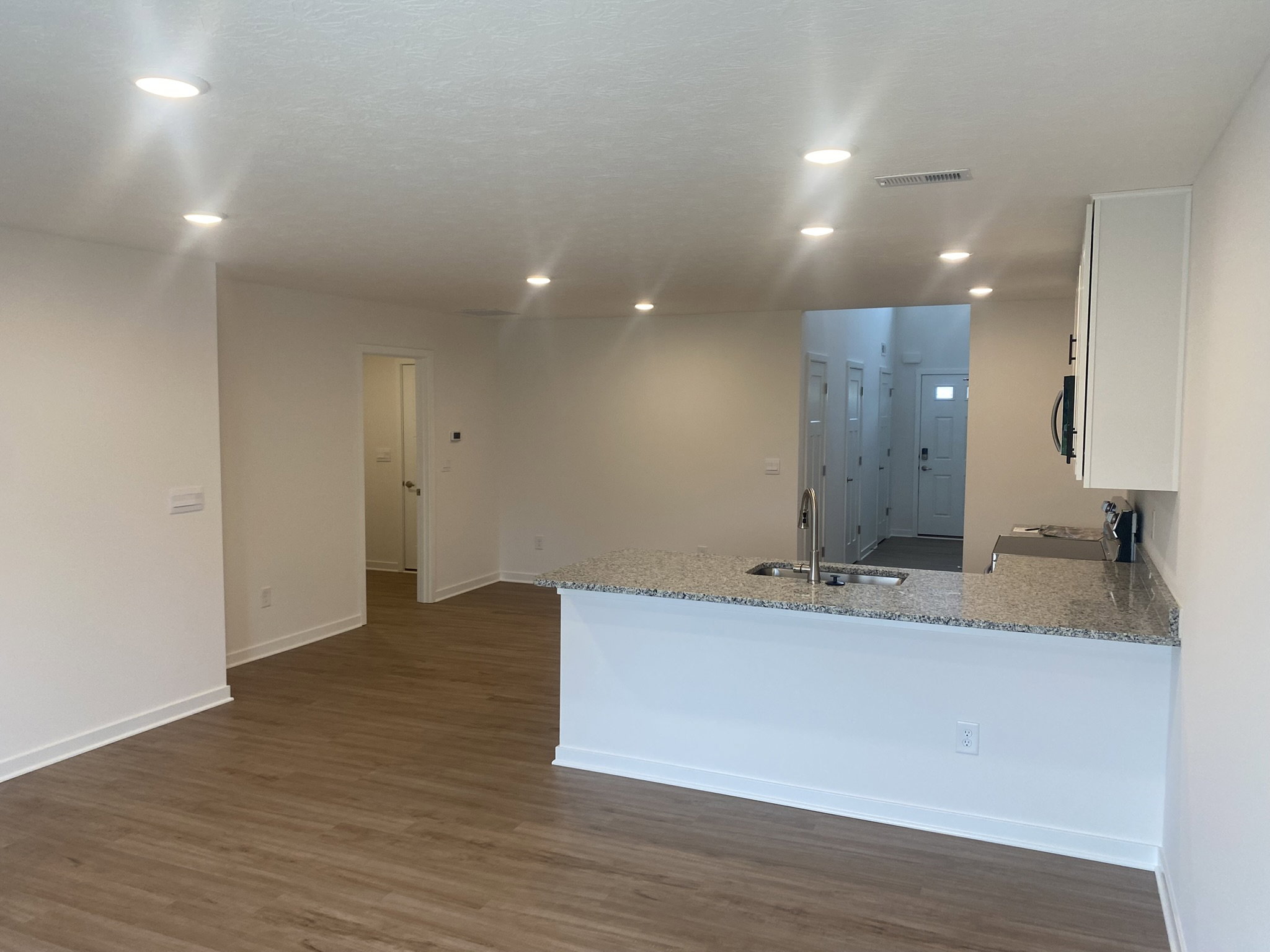 Modern open-concept living space featuring a kitchen with a granite countertop and wooden flooring.