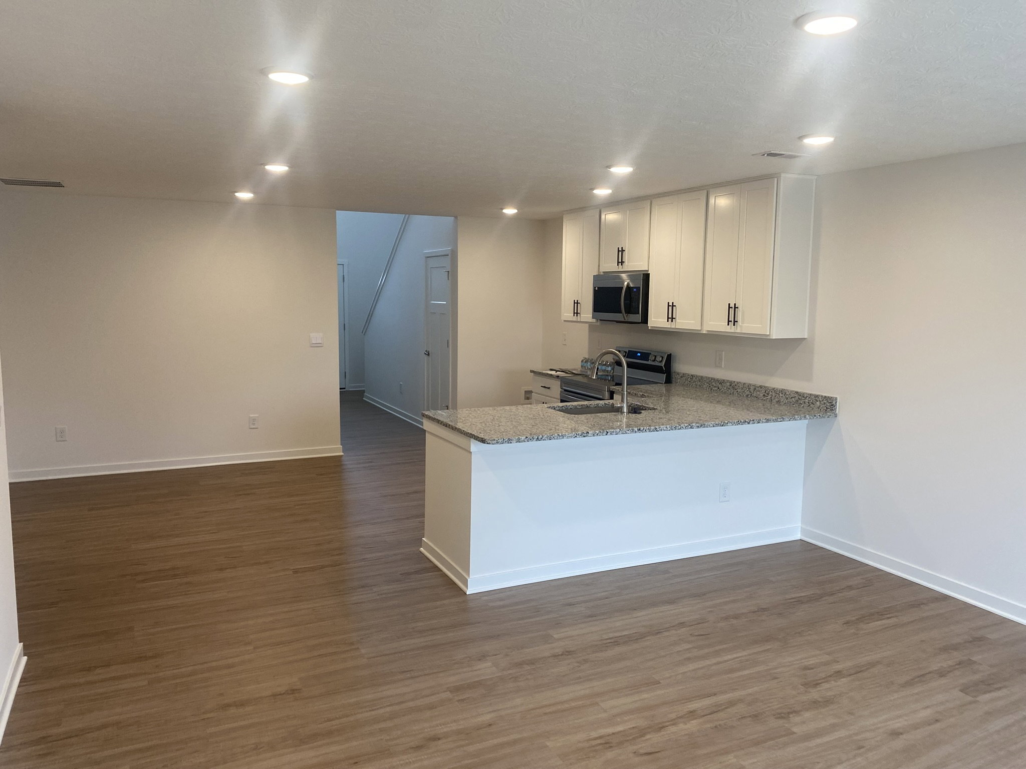 Open-concept living space featuring a kitchen island with granite countertops and modern cabinetry, complemented by warm wood-like flooring.