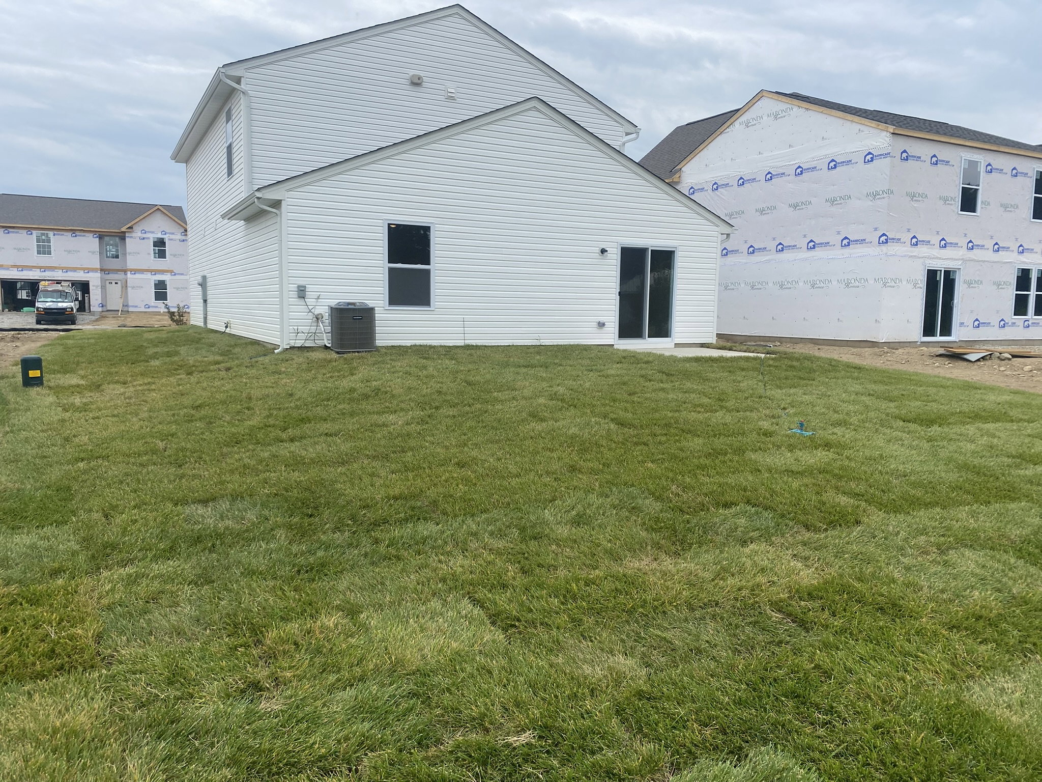 A new white house with a well-manicured lawn, viewed from the backyard, alongside a partially constructed home.