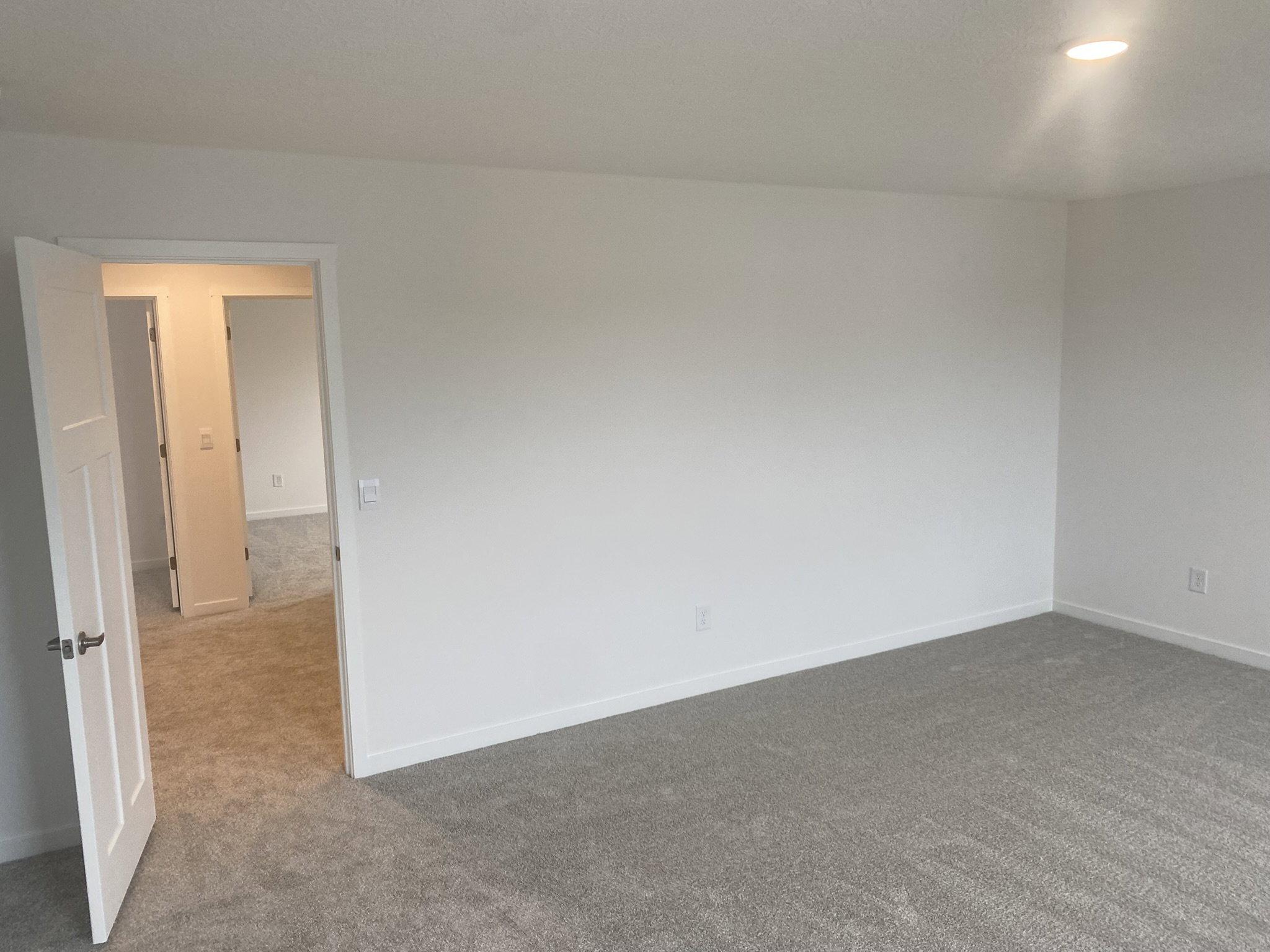 Empty room with light-colored walls and a carpeted floor, featuring an open door leading to another area.