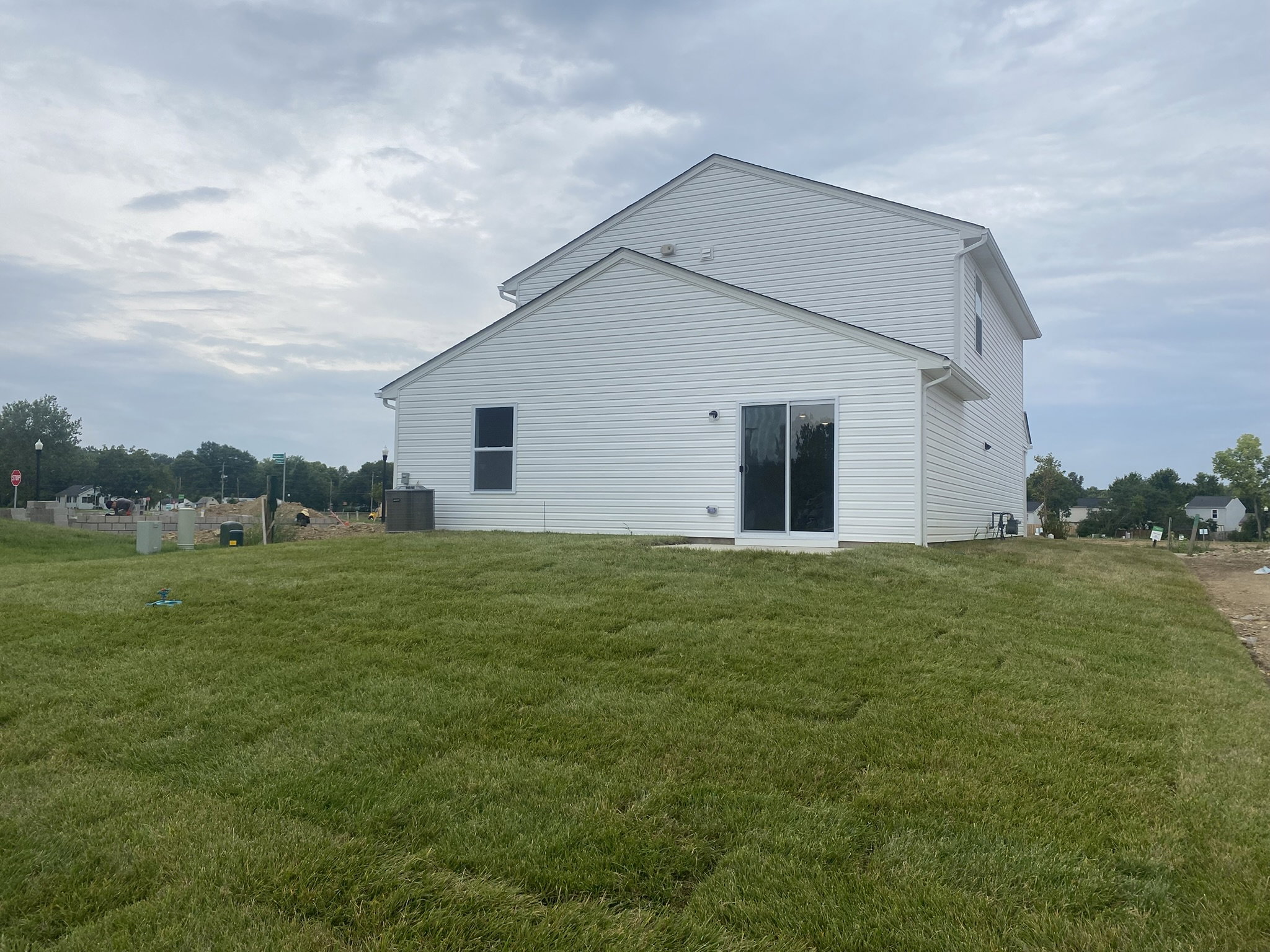 A newly constructed white house with a well-maintained green lawn on a cloudy day.