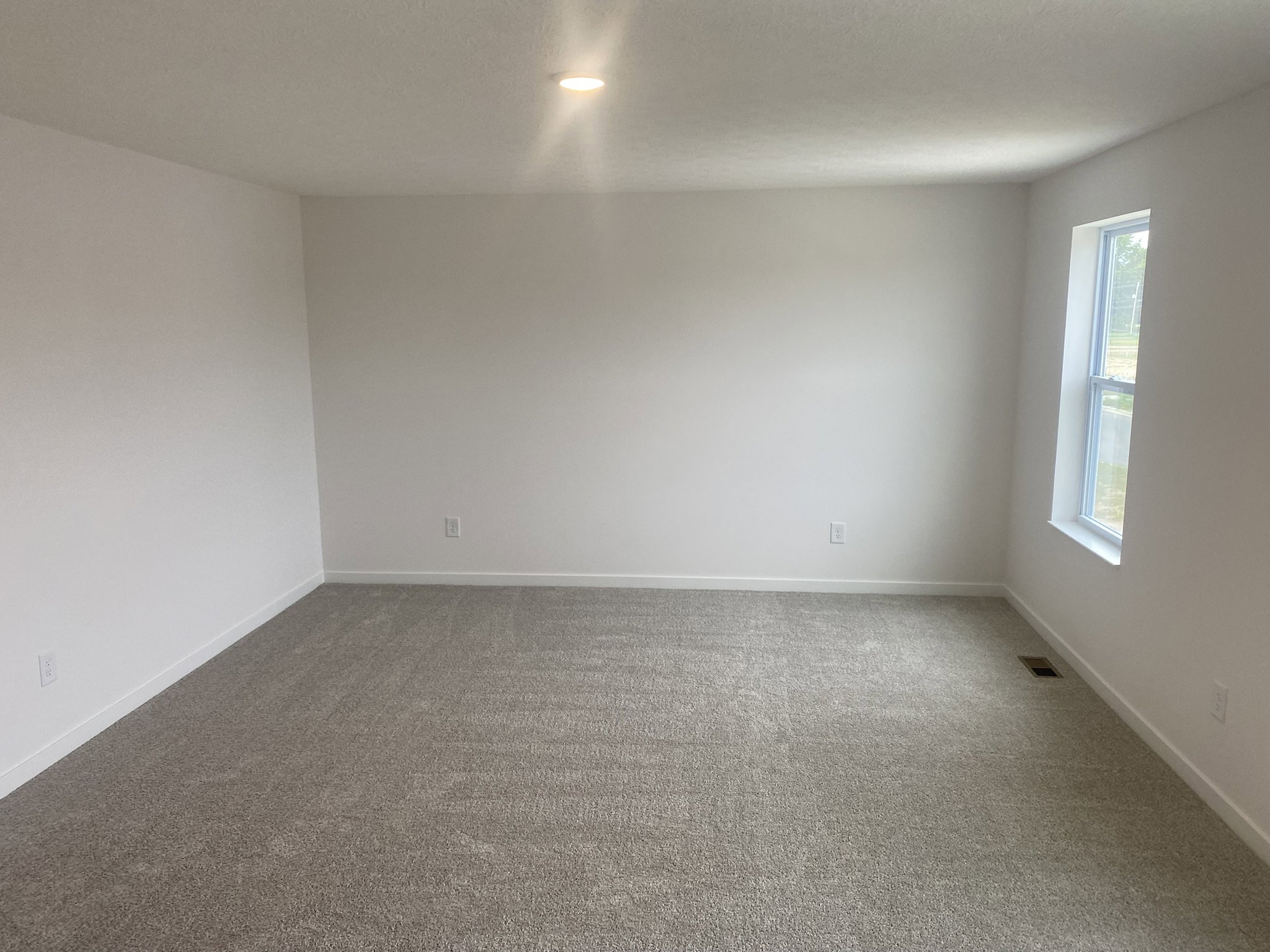 Bright, empty room with gray carpet and white walls, featuring a single window.