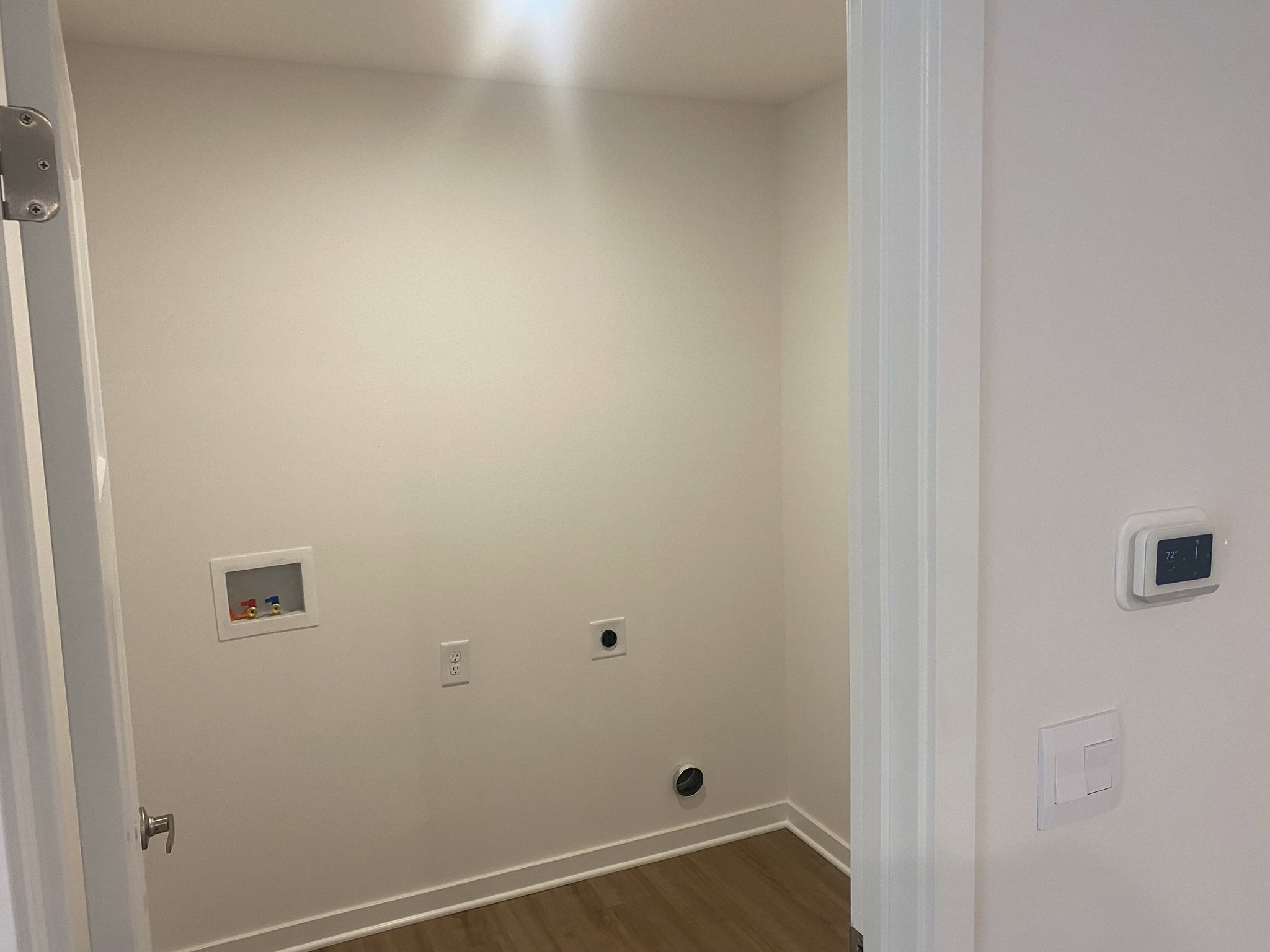 Empty room with a light-colored wall, a thermostat, and a small opening in the wall.