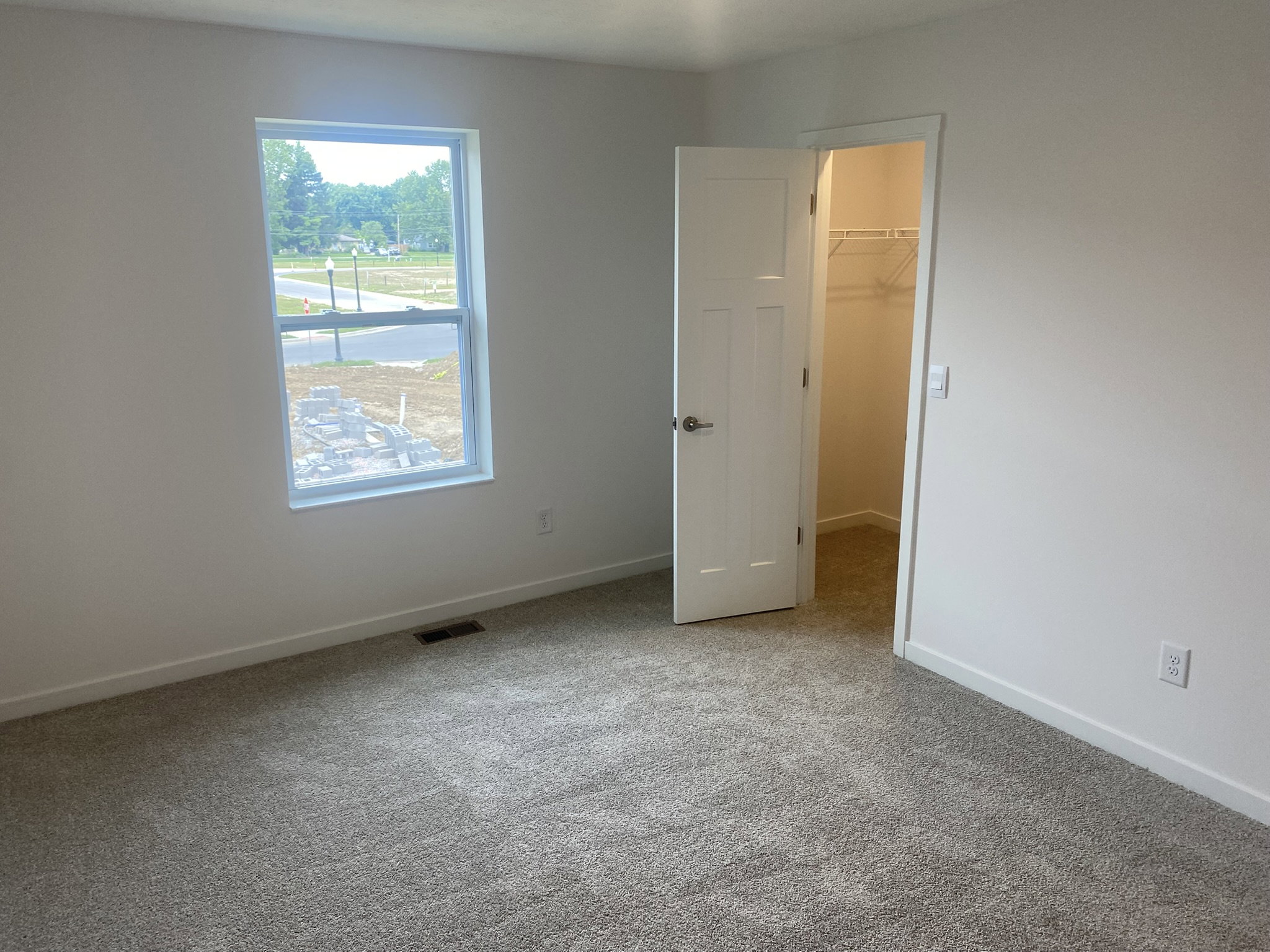 A brightly lit room with beige carpet, featuring an open door leading to a closet.
