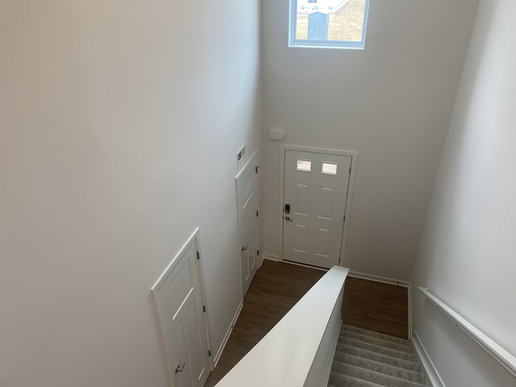 View looking down a staircase toward a white front door and adjacent doors, with a window above.