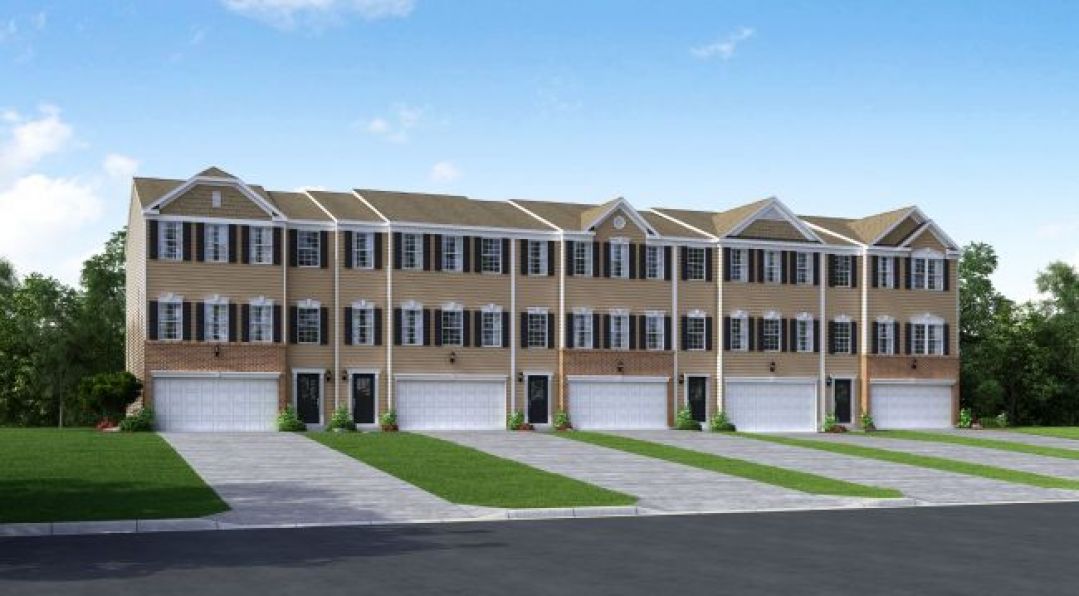 Image of a row of contemporary three-story townhouses with tan siding, white garages, and a landscaped front lawn under a clear blue sky.